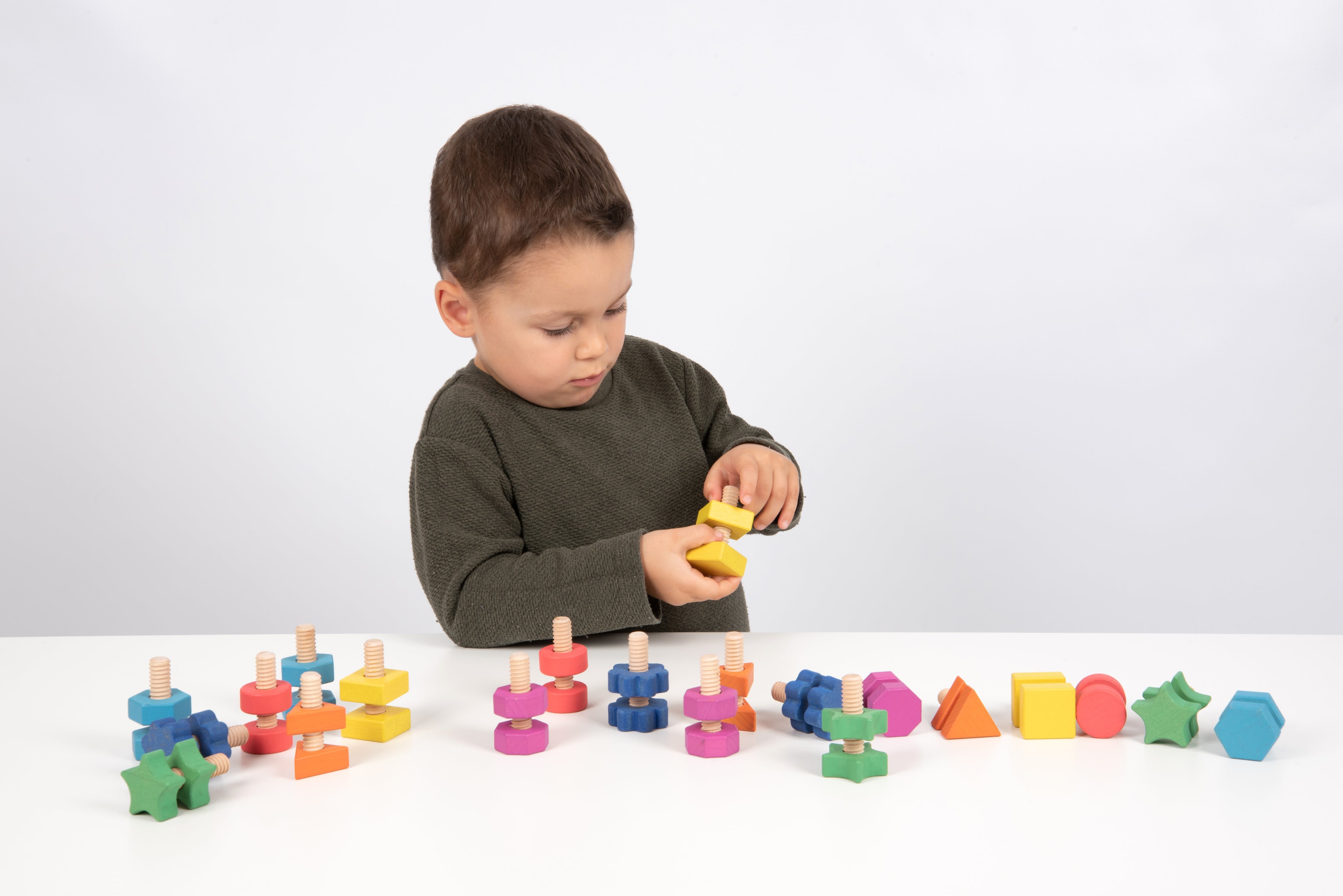 Child reaching for a yellow wooden nut-and-bolt piece among colorful pieces on table