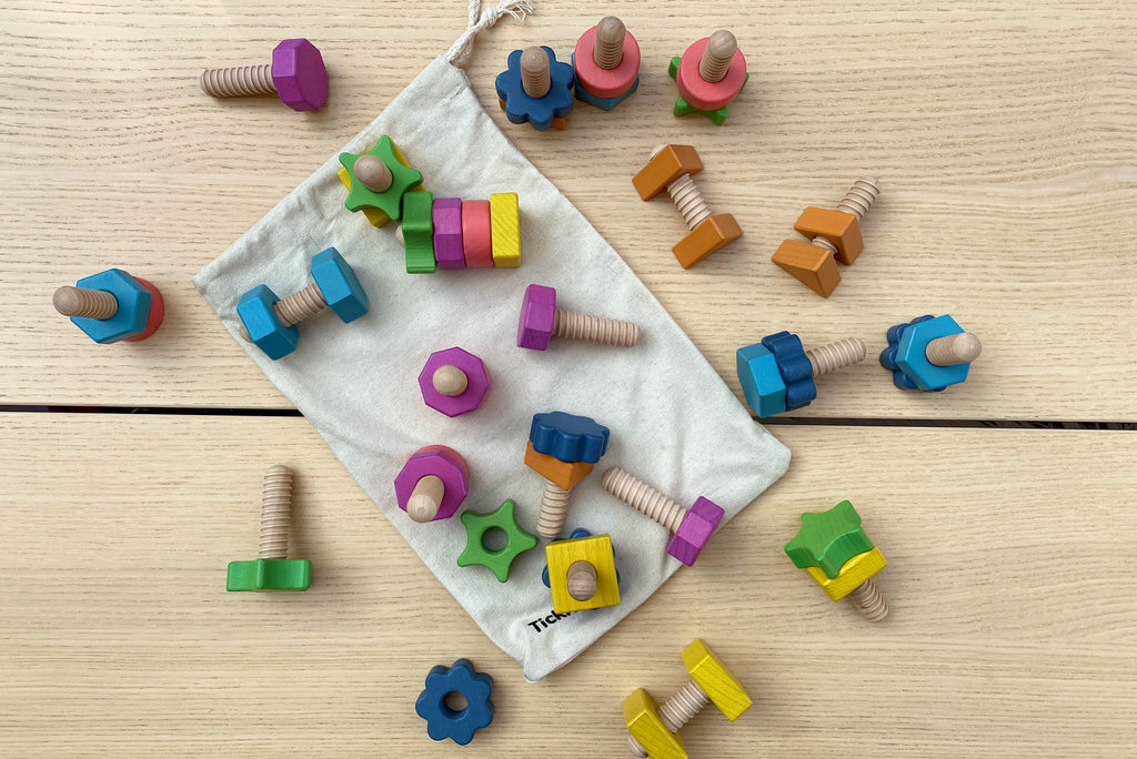 Rainbow wooden nut-and-bolt pieces in a drawstring storage bag, multicolor shapes