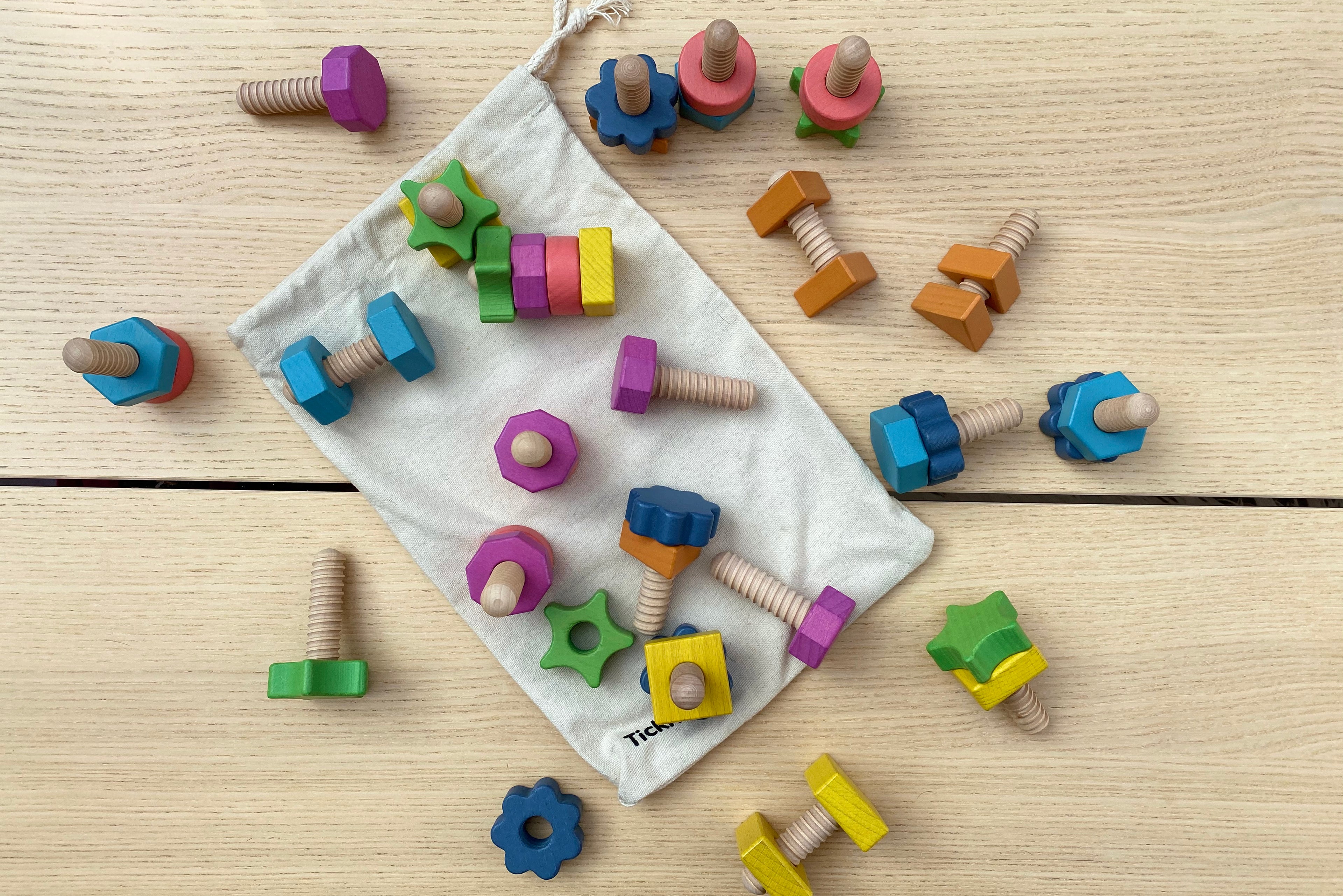 Rainbow wooden nut-and-bolt pieces in a drawstring storage bag, multicolor shapes