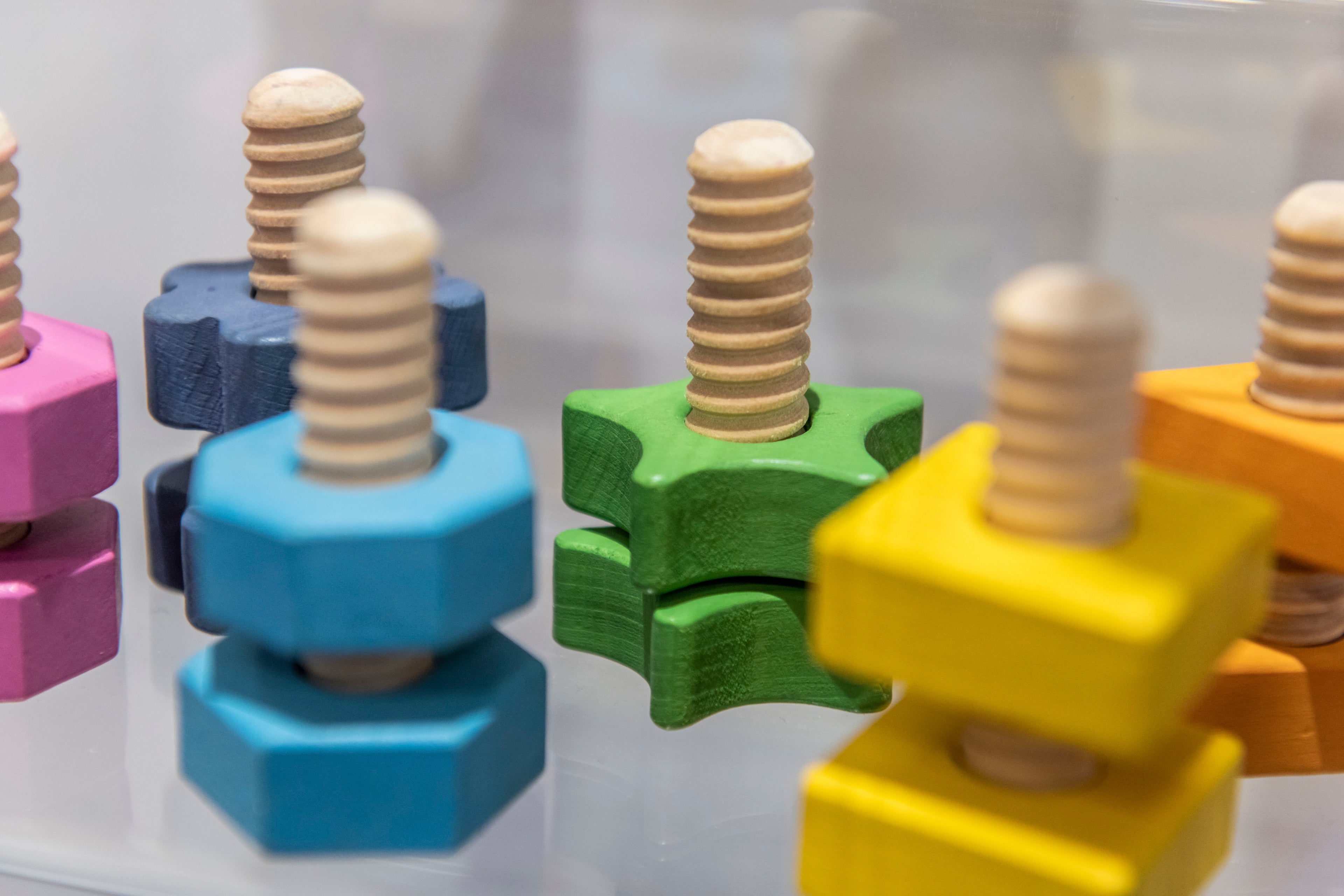 Rainbow wooden nuts and bolts: close view of threaded screws on blue, green, and yellow cubes.