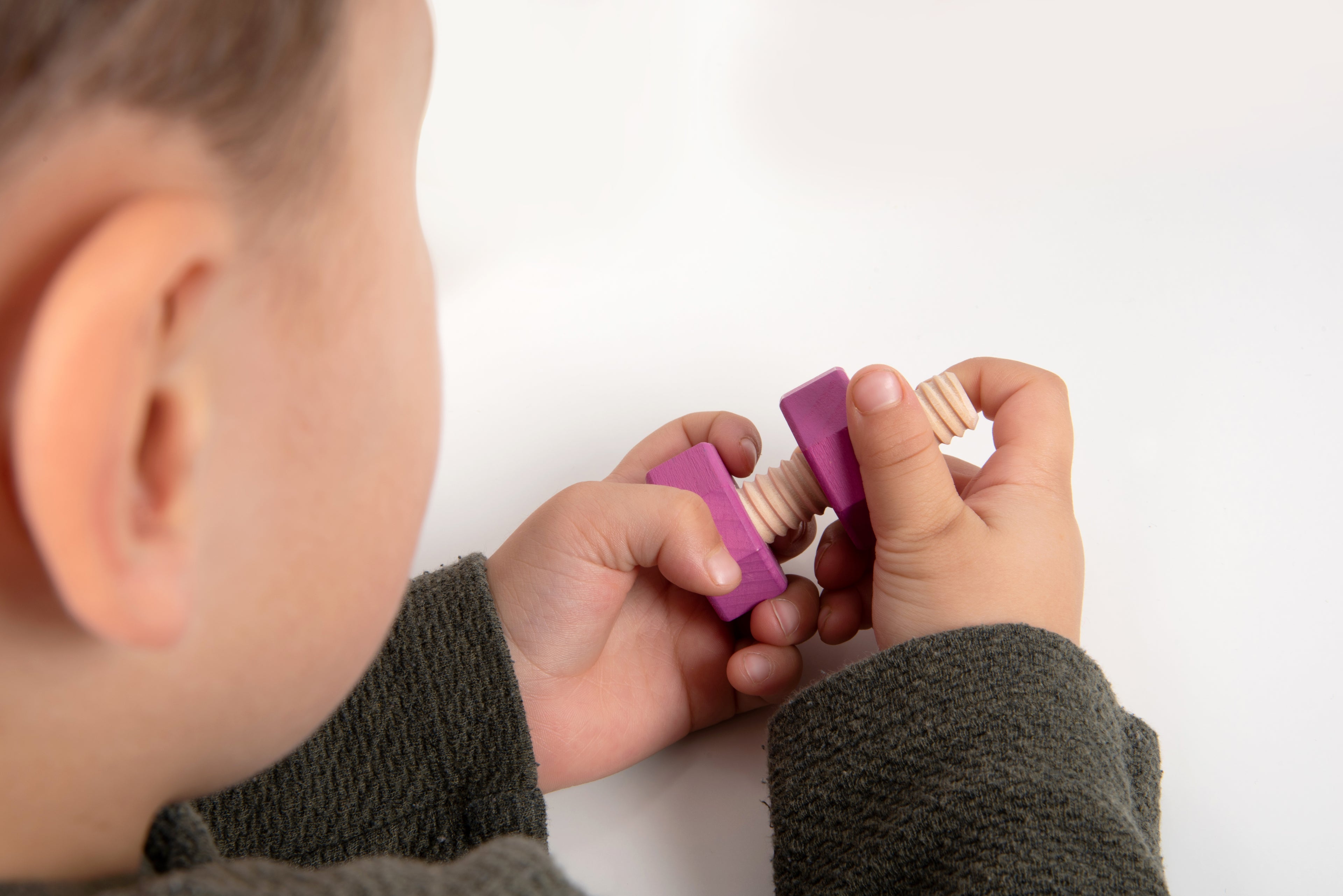 Child hands fitting a purple wooden bolt into a matching nut from the rainbow set.