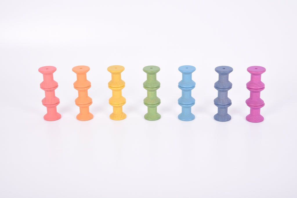 Wooden thread spools row in seven pastel colors: pink, orange, yellow, green, blue, indigo, purple