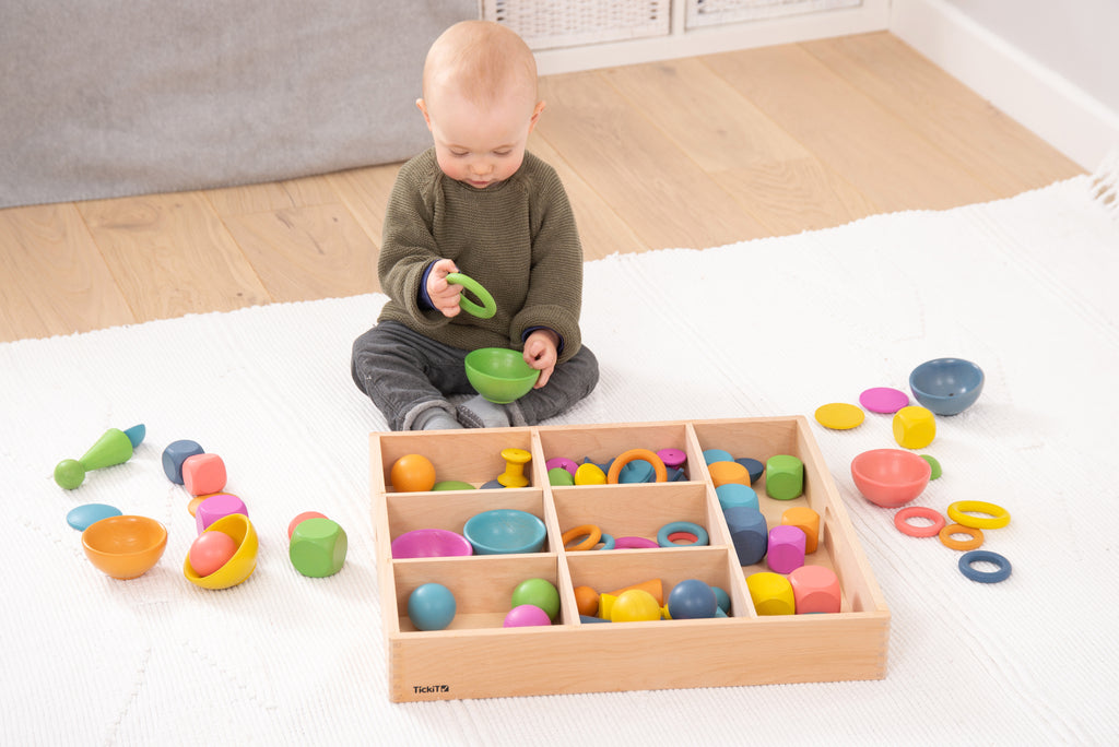 Wooden sorting tray with multicolor wooden rings and cups; child holds a green piece