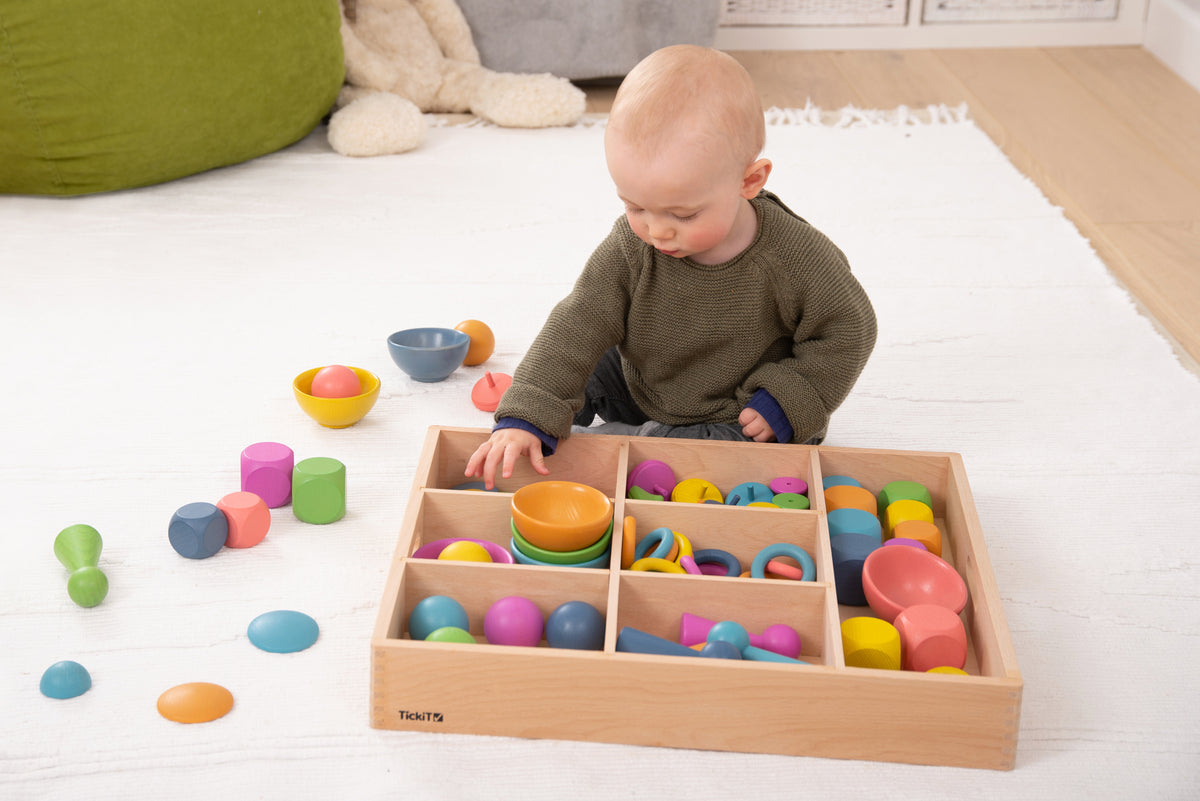 Wooden divider tray filled with colorful wooden rings, bowls, and discs for sorting