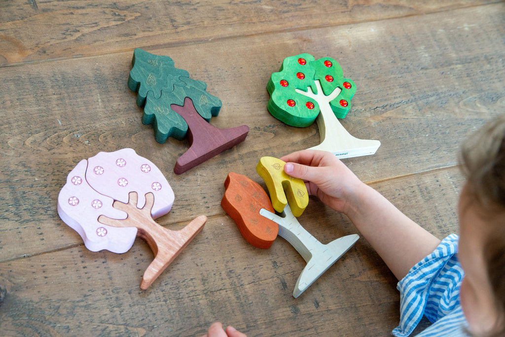 Assorted wooden tree puzzle pieces, including pink and green trees, on a table