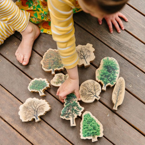 Wooden tree-shaped activity pieces with painted green and beige leaves on a gray board