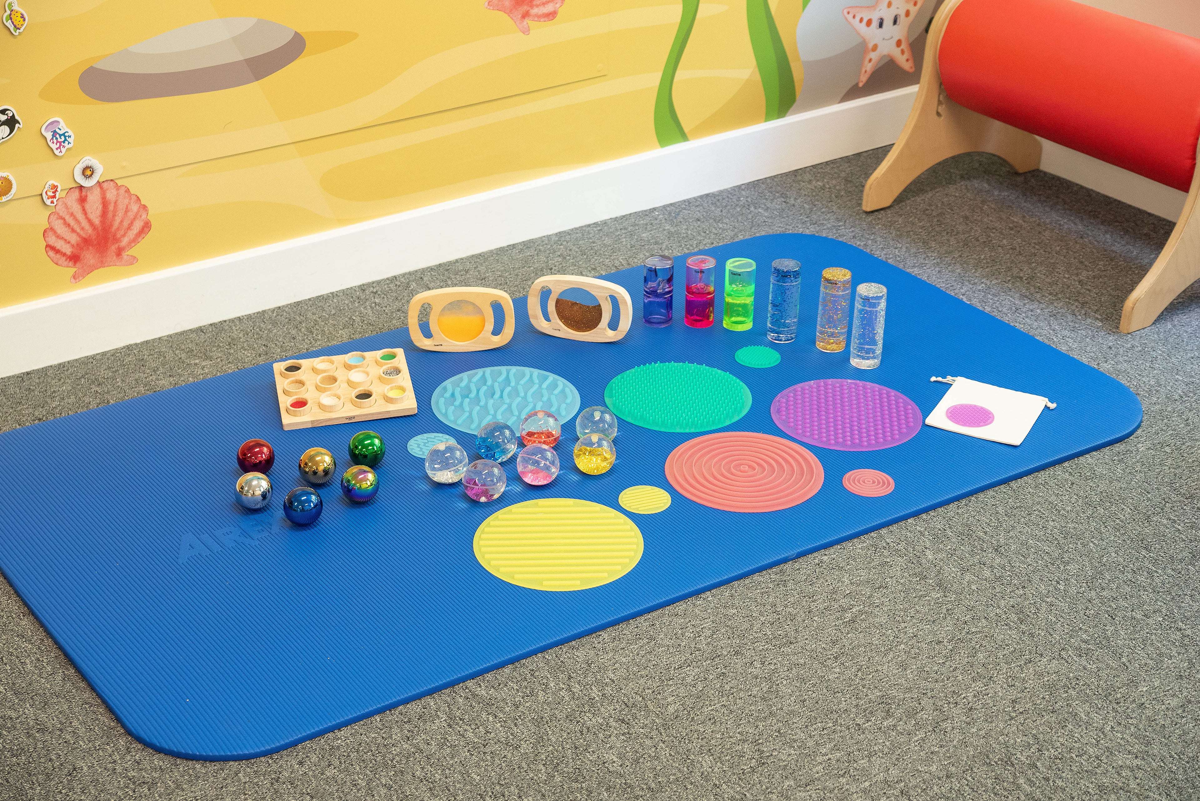 Blue sensory mat with tactile discs, small jars, and bead balls arranged on floor