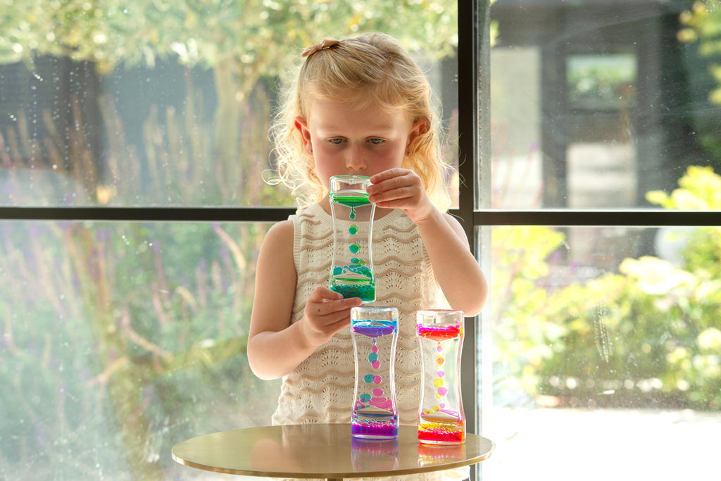 Child holding a rainbow sand timer; colorful bead cascades in a clear hourglass tube