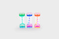 Three translucent rainbow sand timers with colored bead cascades: green, pink, blue