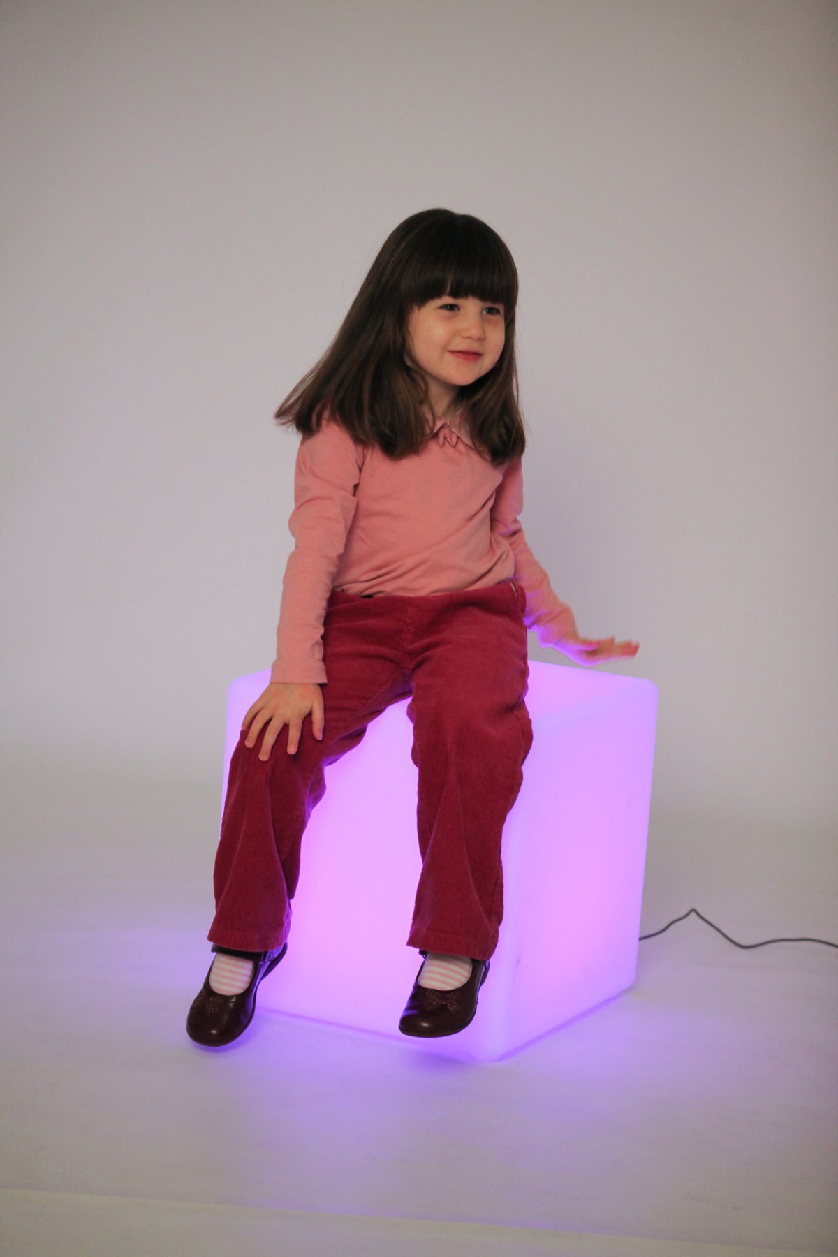 Light-up cube lamp with purple glow, child standing and smiling