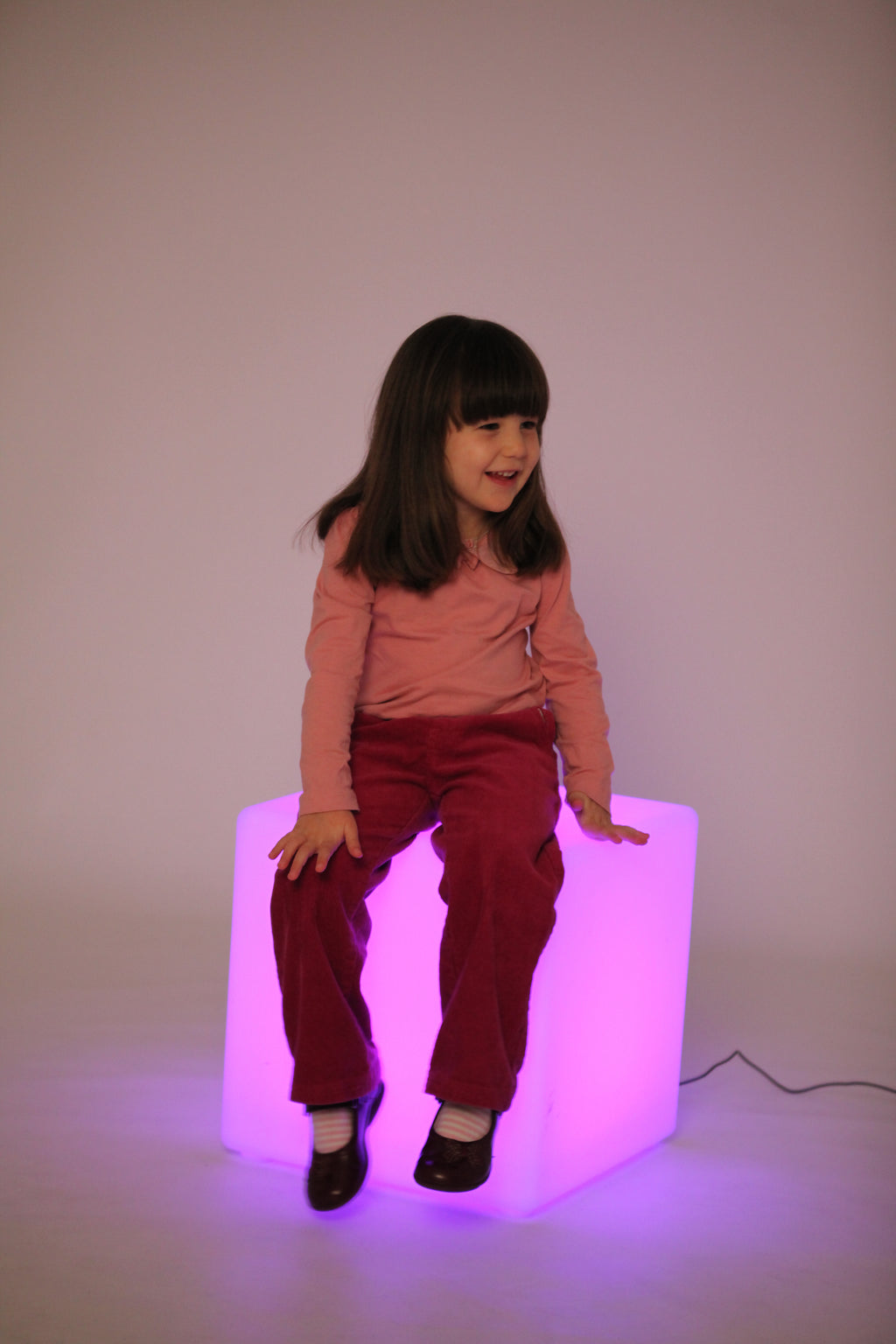 Light-up cube lamp with pink-purple glow, child sitting beside