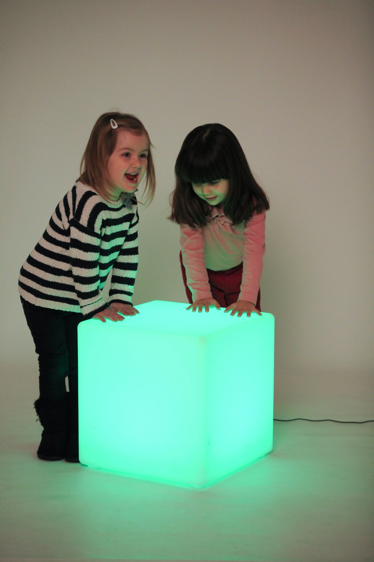 Light-up cube lamp glowing turquoise, two children watching