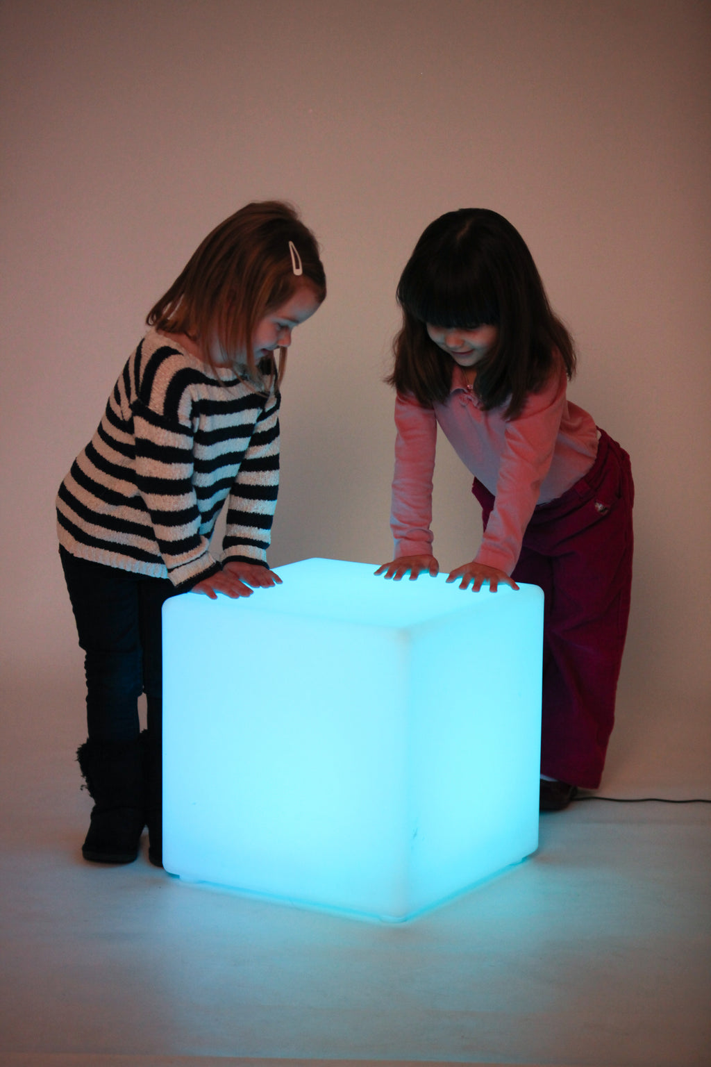 Light-up cube lamp glowing light blue, two children leaning on top