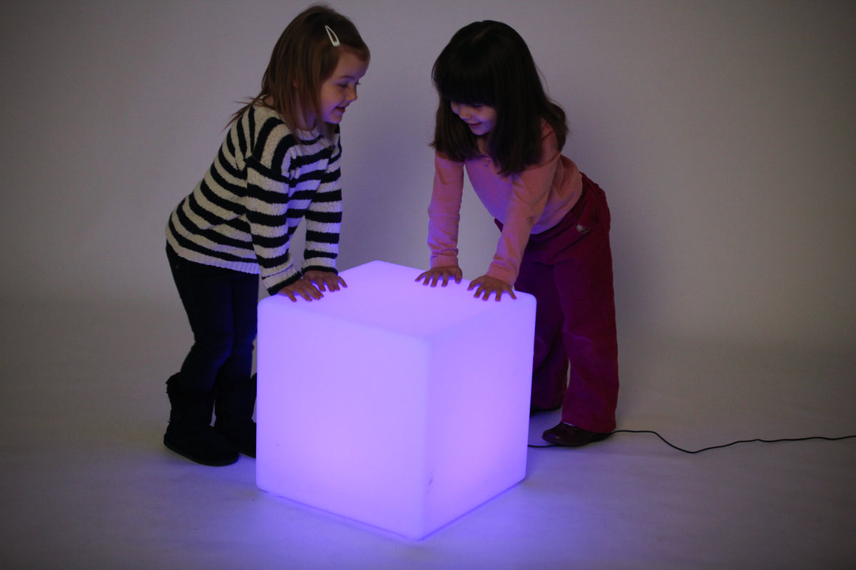 Light-up cube lamp glowing violet, two children reaching toward top