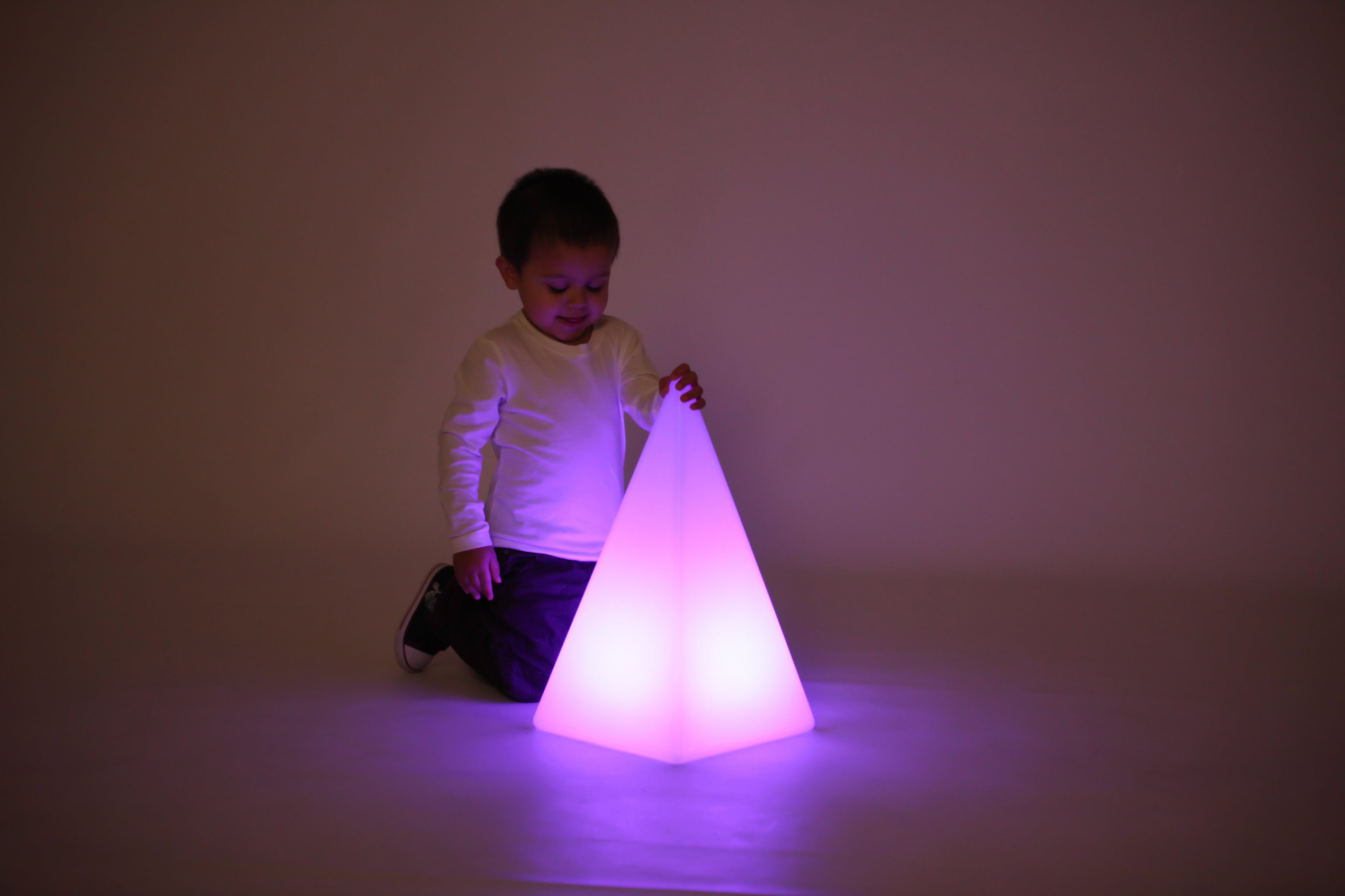 Child playing with glowing light pyramid, purple light casting
