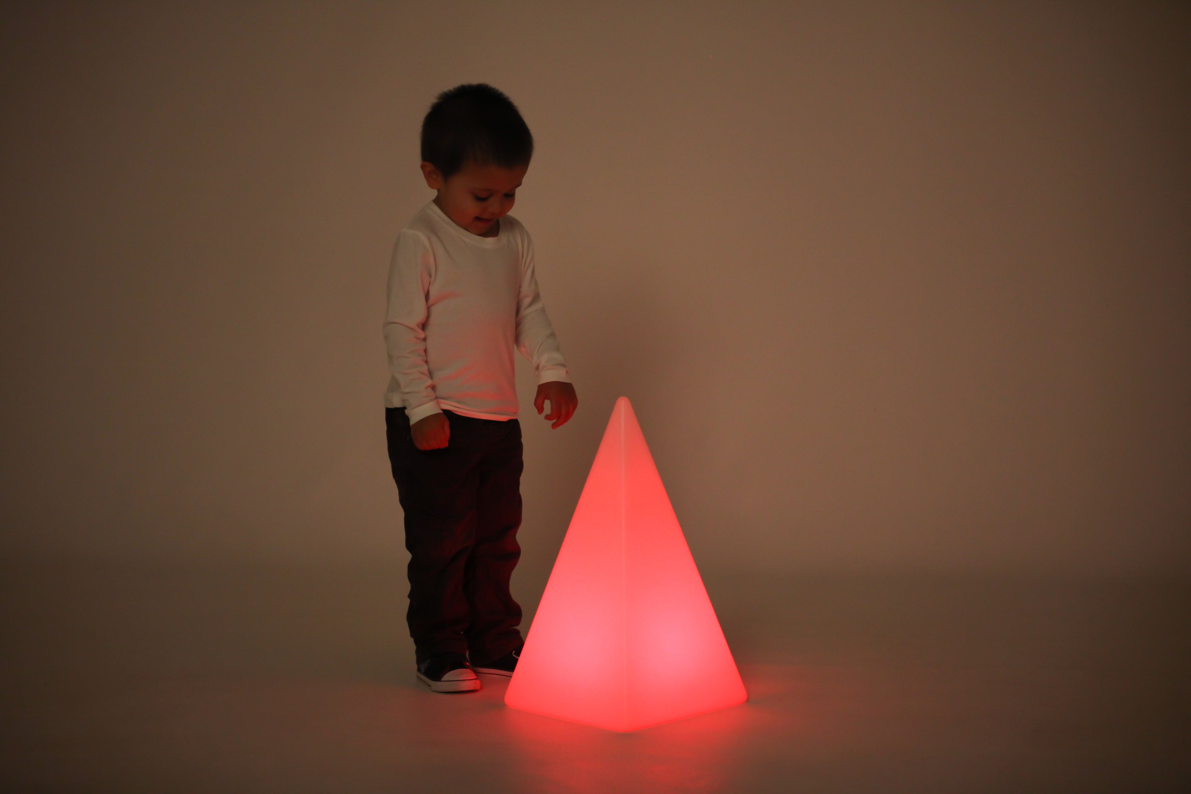 Child standing by glowing light pyramid, red light casting