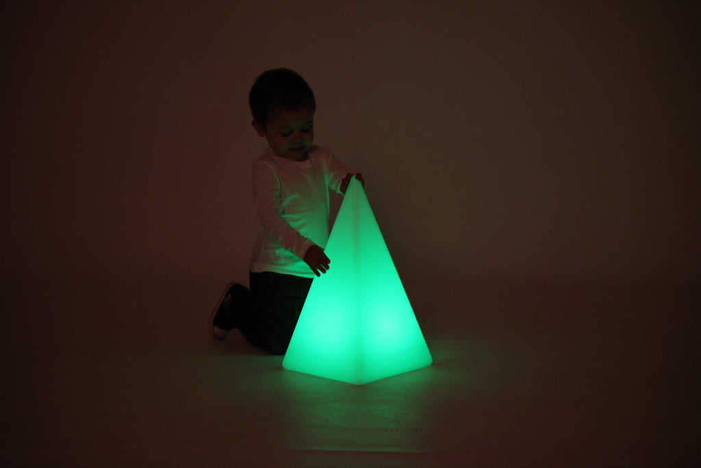 Child playing beside glowing light pyramid, green light
