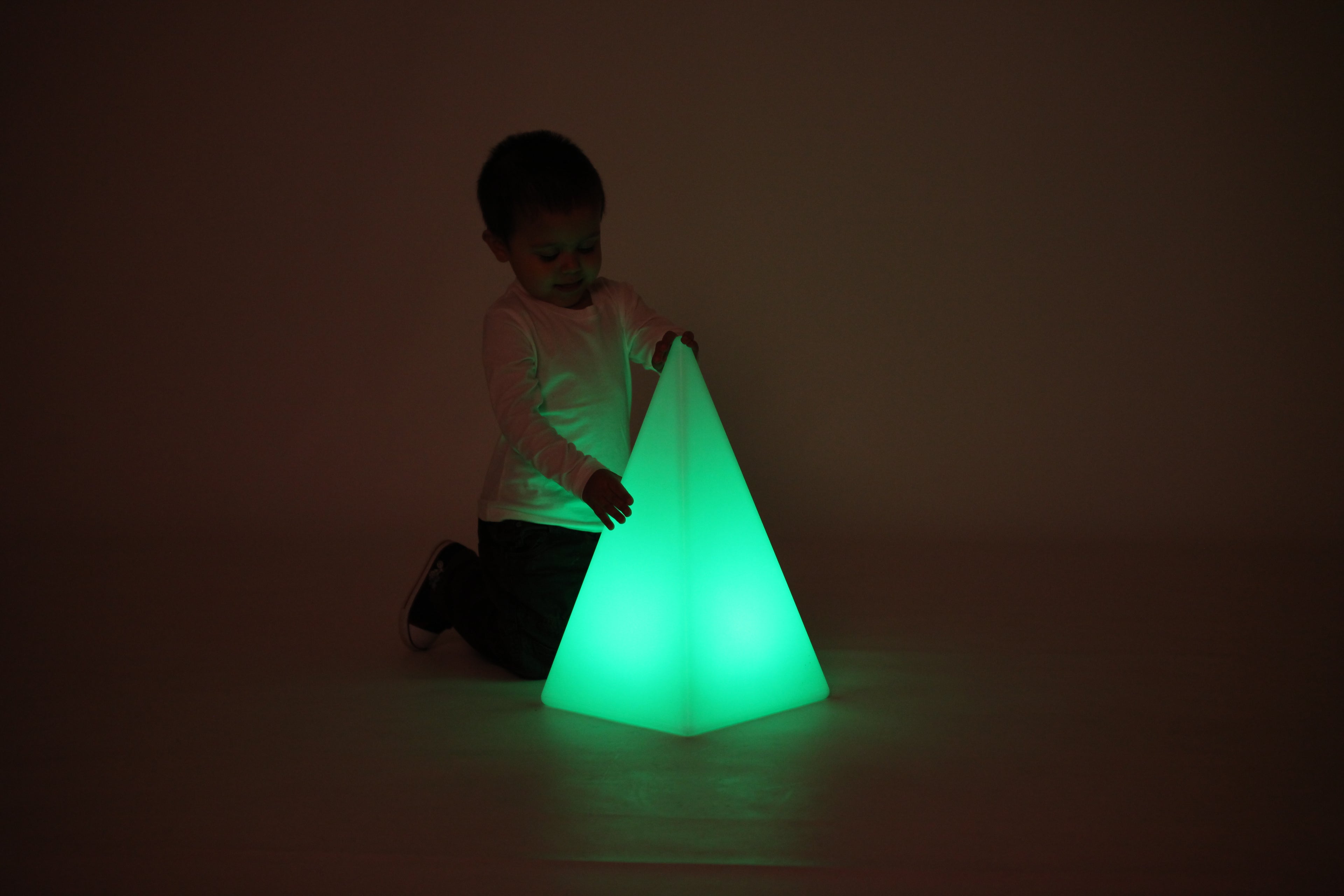 Child playing beside glowing light pyramid, green light