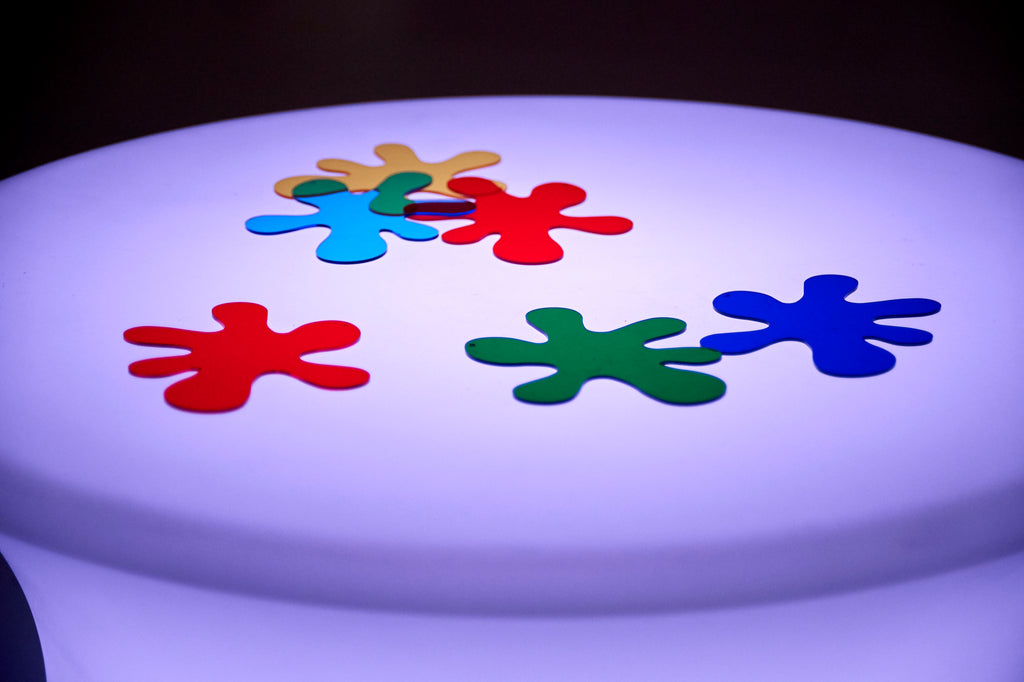 Sensory glow table with a round illuminated white top featuring multicolor puzzle-piece shapes