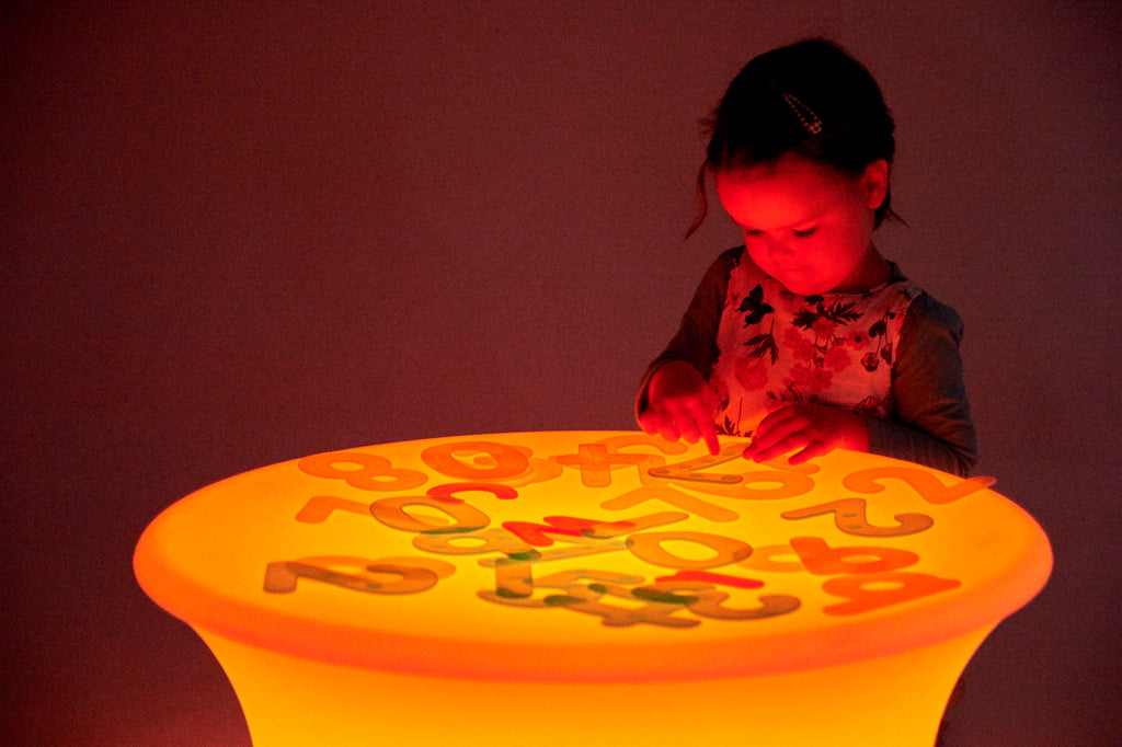 Sensory glow table with an orange-glowing round top and colorful number shapes