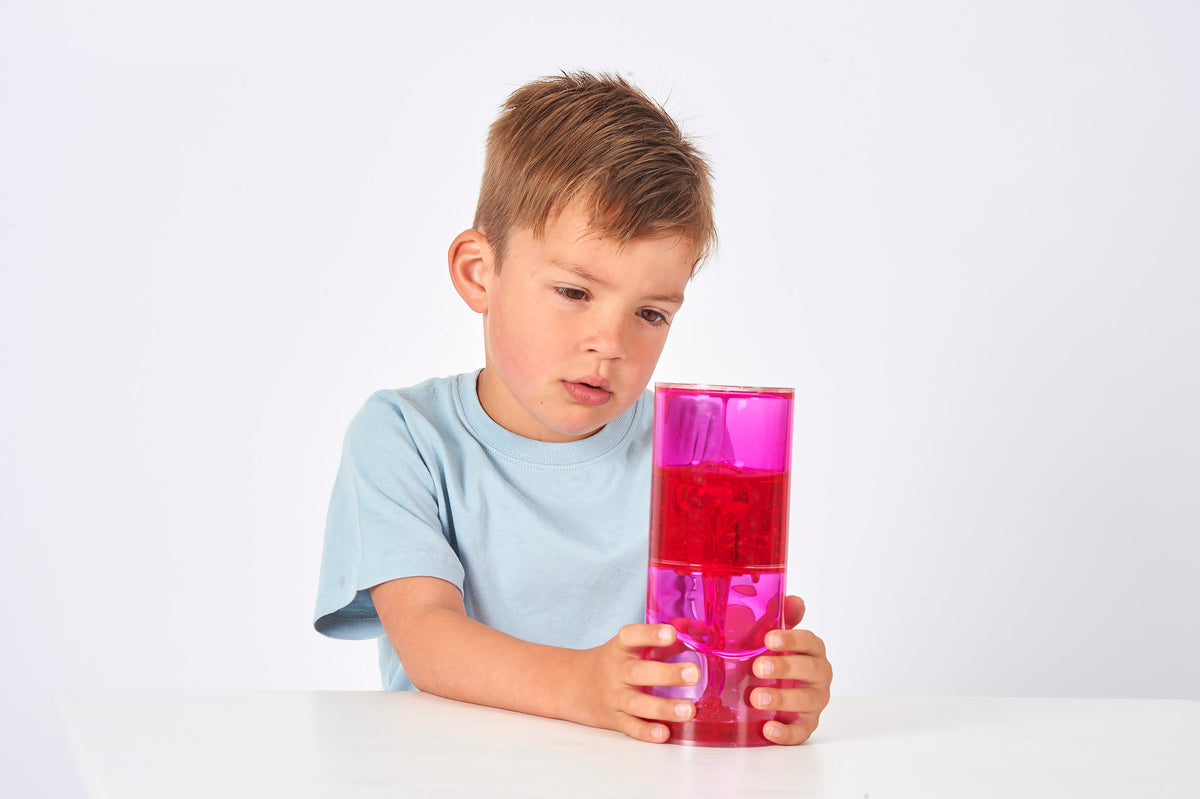 Sensory jumbo ooze tube with bright pink translucent gel, held while seated.