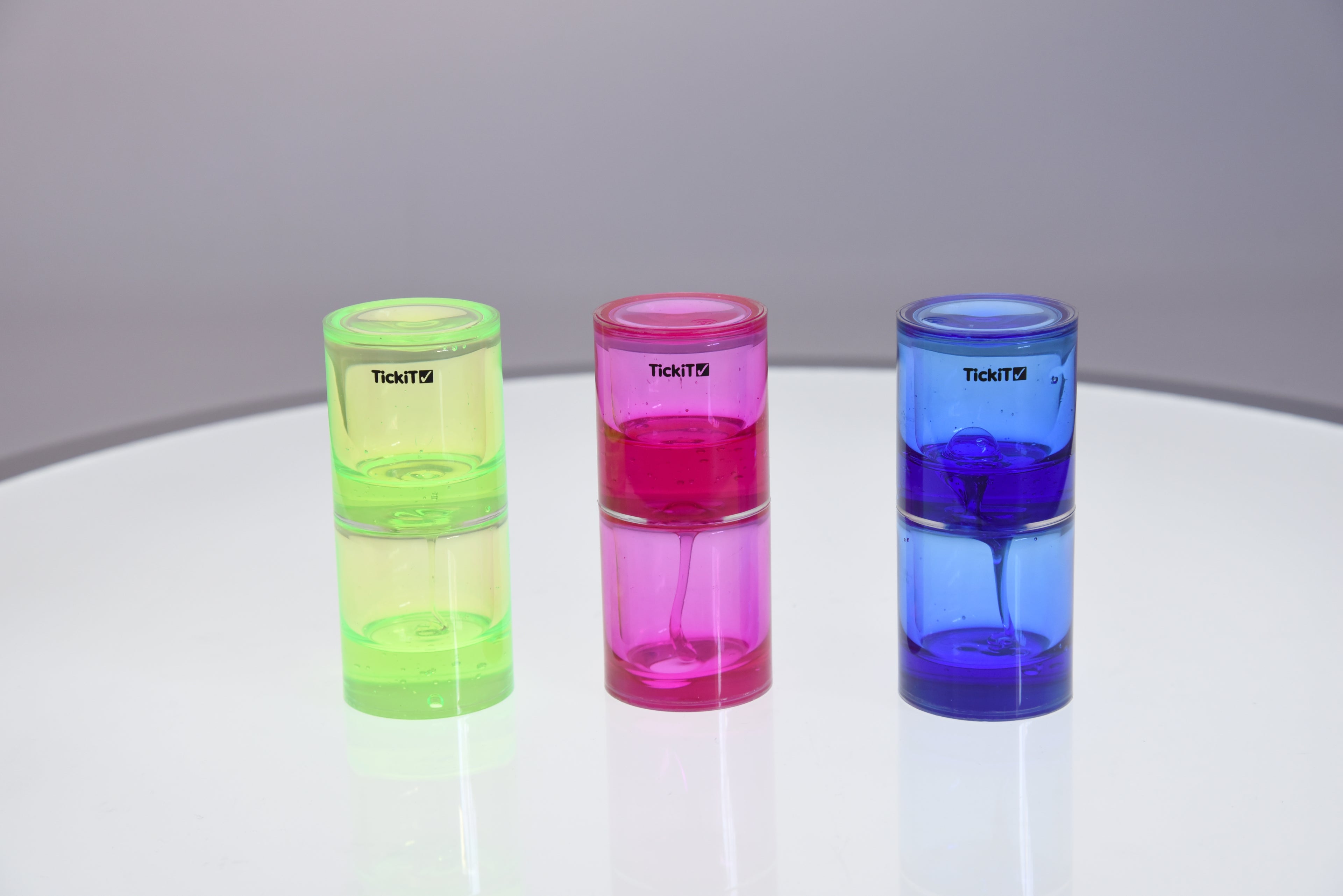 Three tickit ooze tubes: lime green, pink, and blue on reflective surface