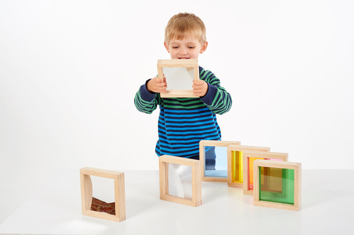 Child holding a wooden square sensory block with clear and colored panels