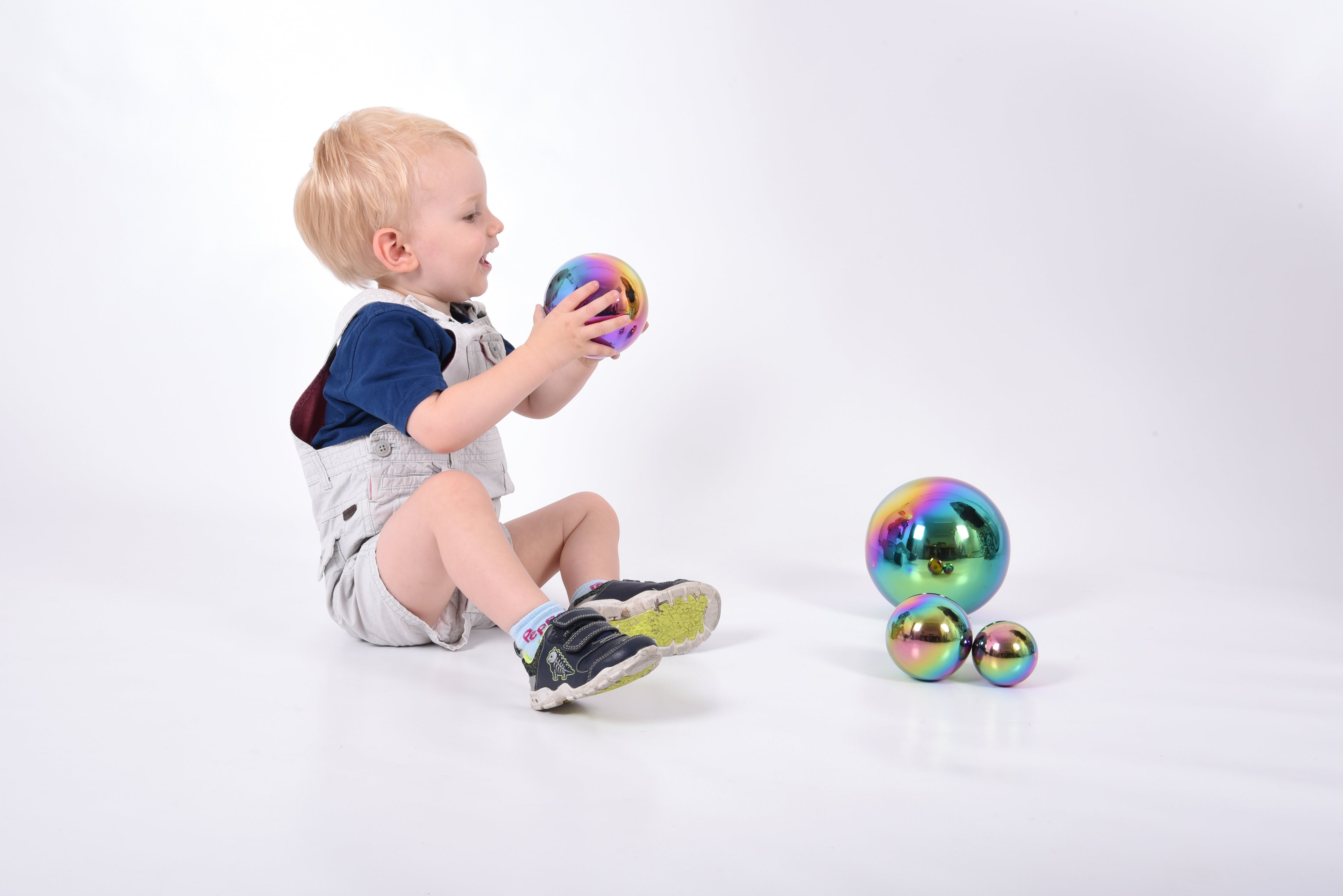Set of four iridescent metallic balls with rainbow sheen, child holds one with three nearby