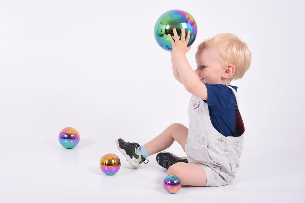 Set of four iridescent metallic sensory balls with rainbow sheen, one held overhead by a child
