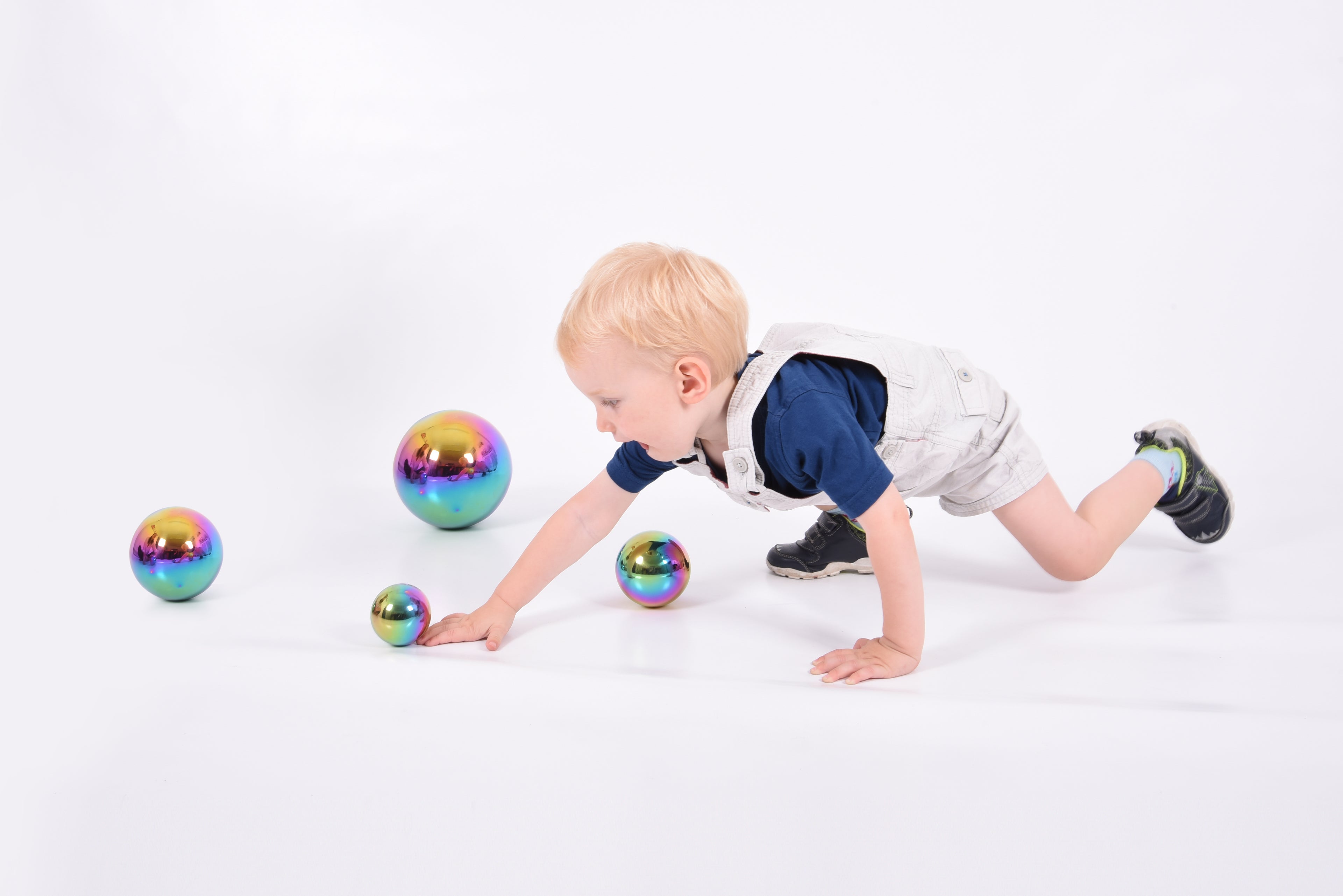 Set of four iridescent metallic balls with rainbow sheen for sensory play, child reaching