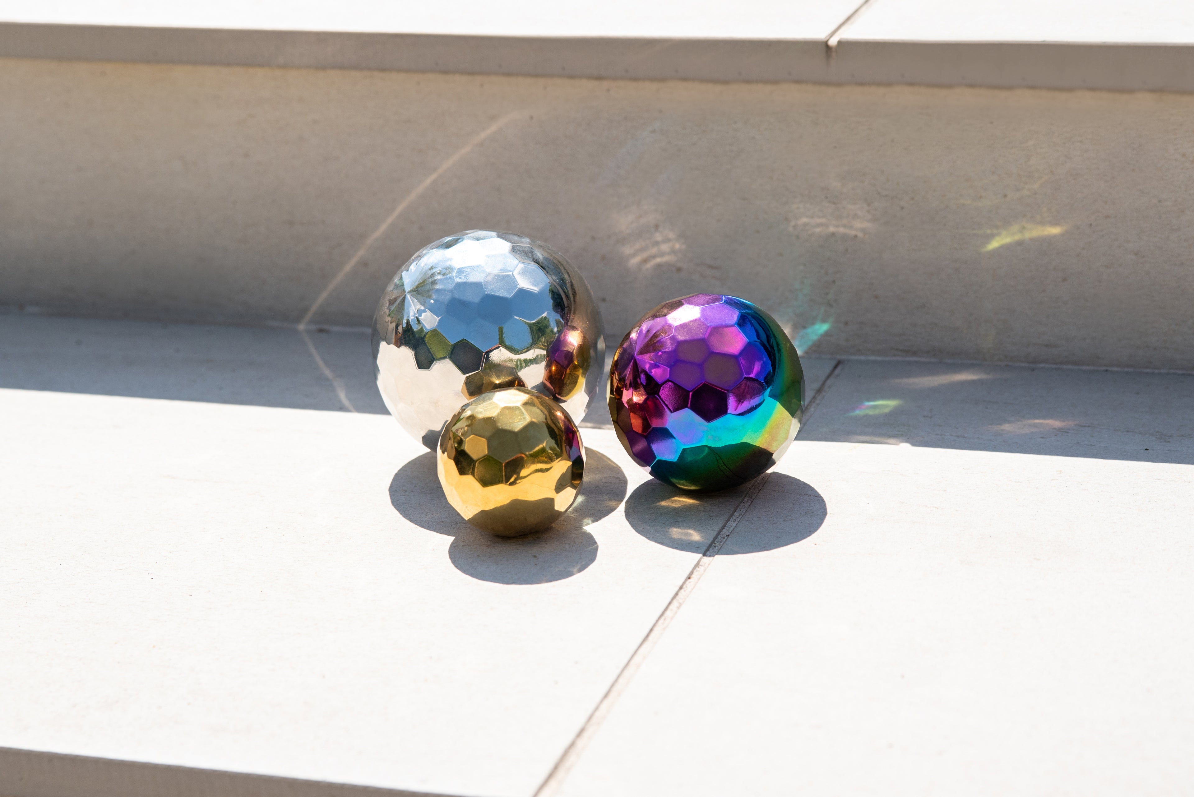 Three iridescent metallic mosaic balls: silver, rainbow-purple, and gold