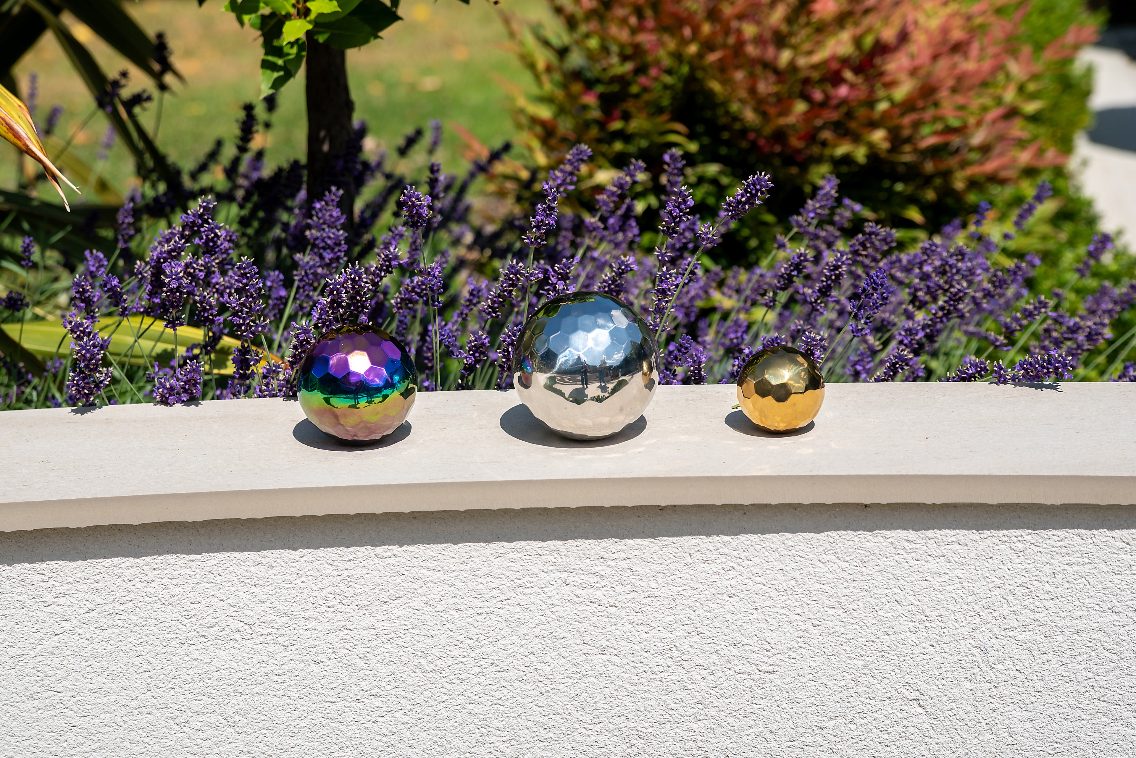 Three iridescent metallic mosaic balls: rainbow, silver, and gold on ledge