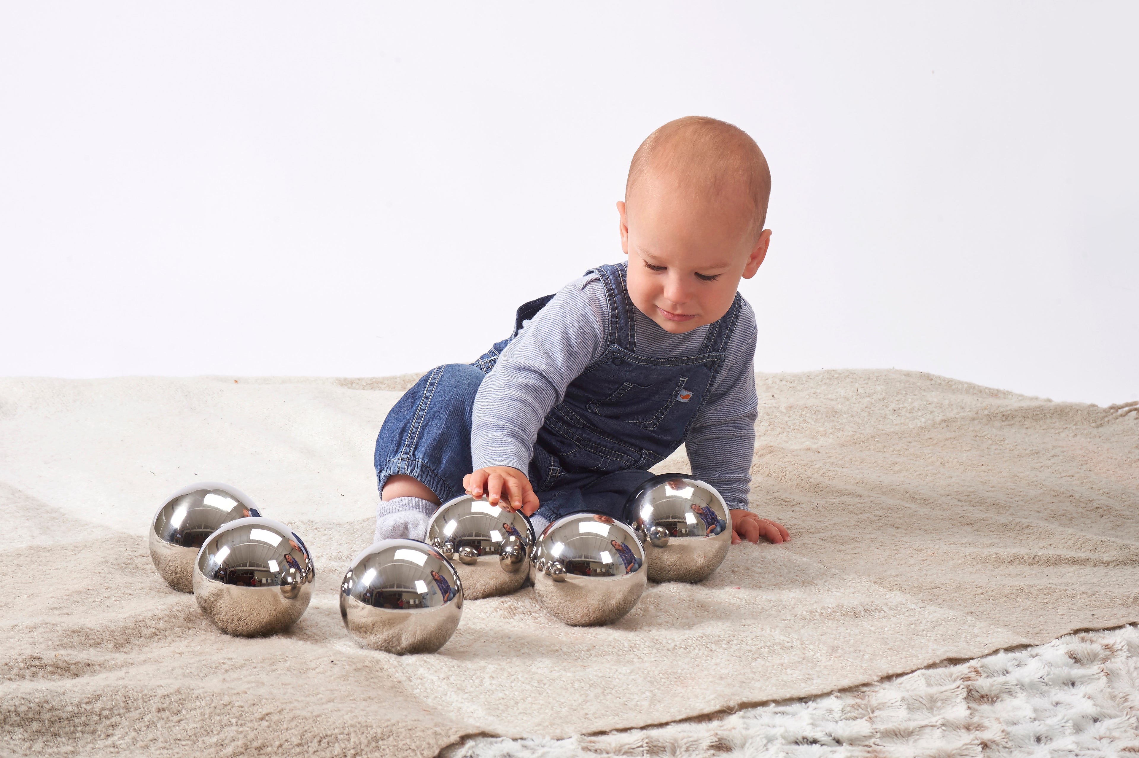Set of six shiny steel sensory balls, baby leaning forward with balls around.
