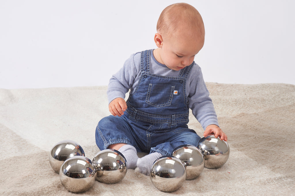 Set of six shiny steel balls for sensory play, baby reaching toward one ball.