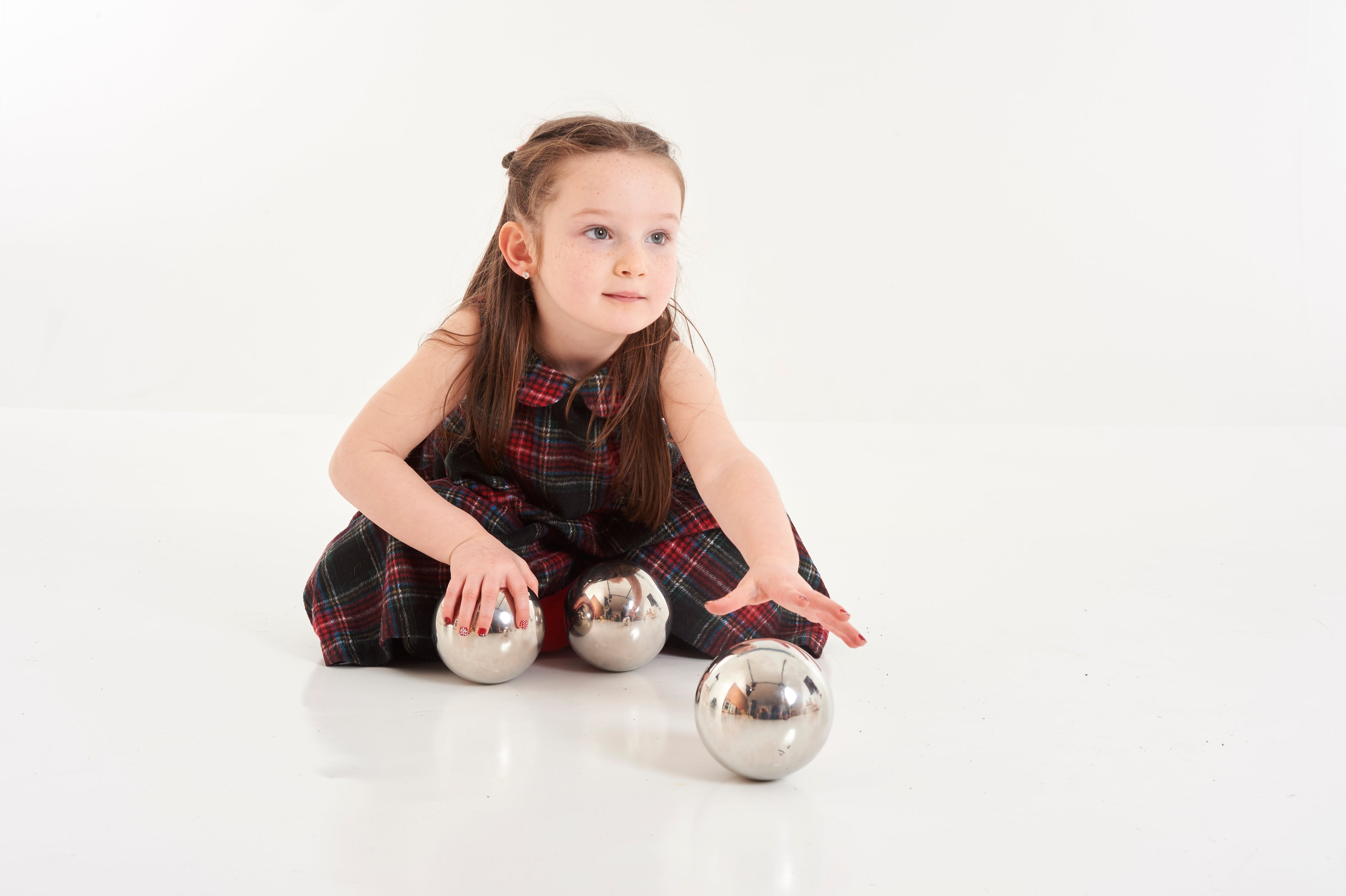 Set of six shiny steel balls for sensory play, child seated holding a ball.