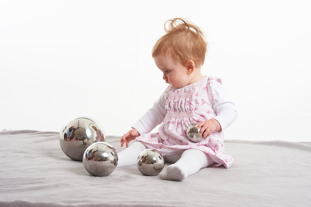Set of shiny silver steel sensory balls with reflective surfaces; baby kneeling and playing