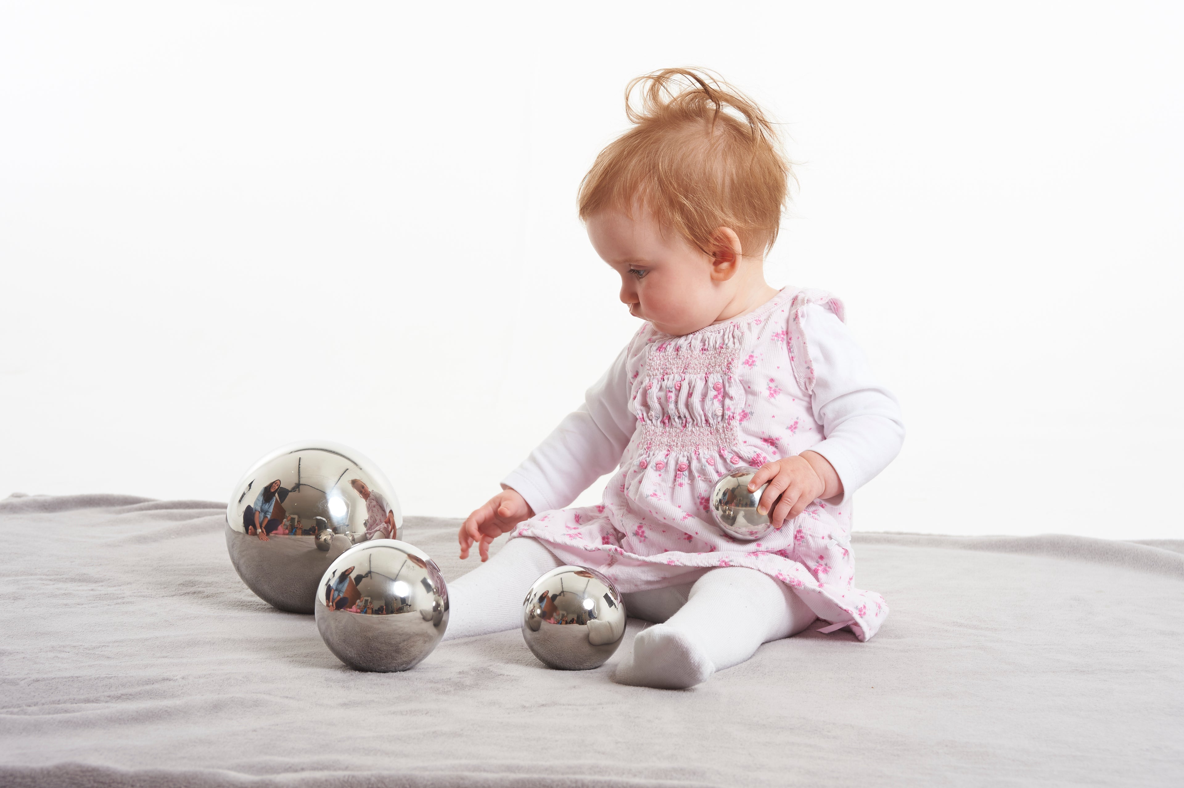 Set of shiny silver steel sensory balls with reflective surfaces; baby kneeling and playing