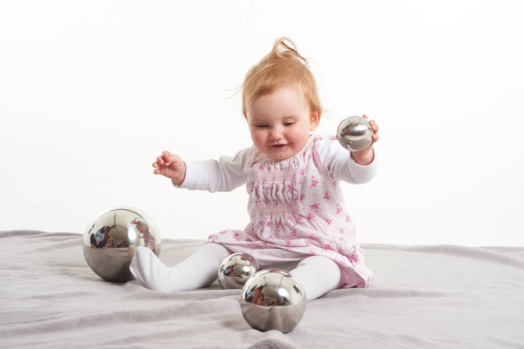 Baby playing with shiny silver steel sensory balls, holding one and surrounded by others