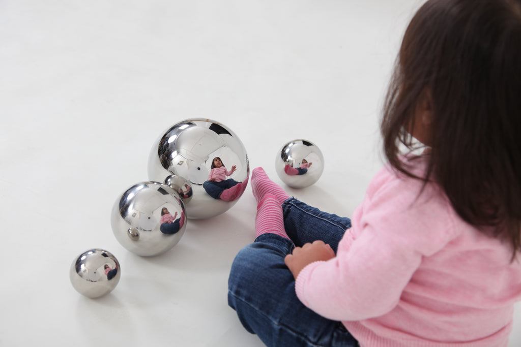 Shiny silver steel sensory balls arranged near a child’s knees in pink