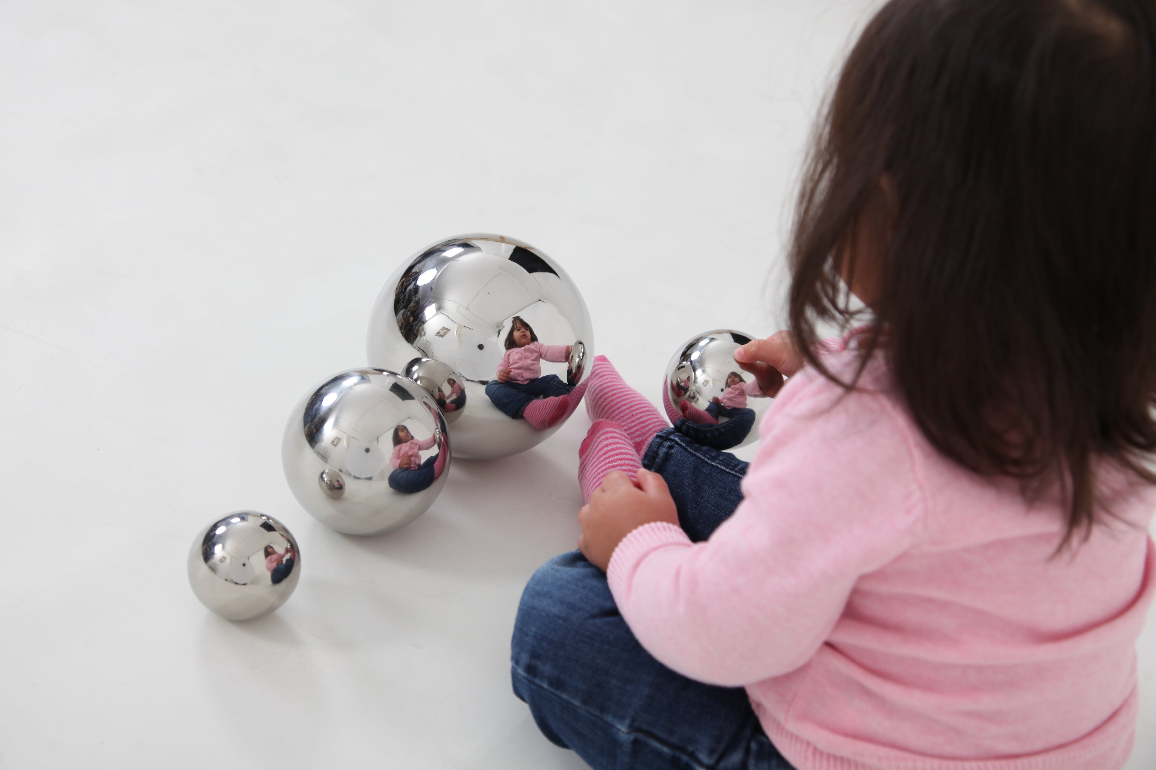 Child in pink sweater interacting with shiny silver steel sensory balls on the floor