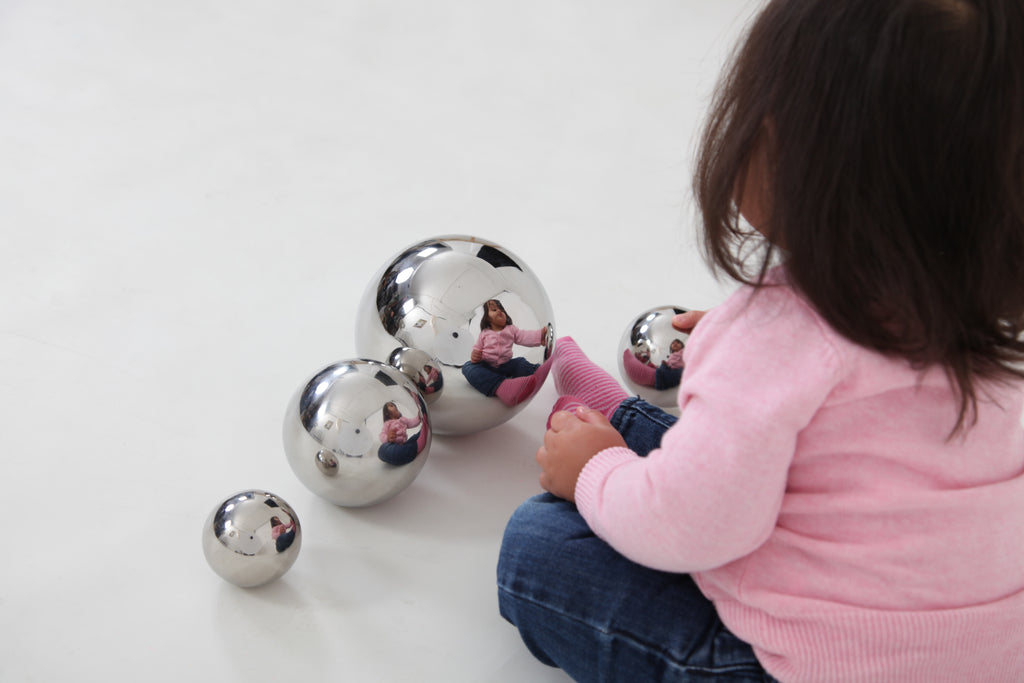 Four shiny silver steel sensory balls beside a child in a pink sweater