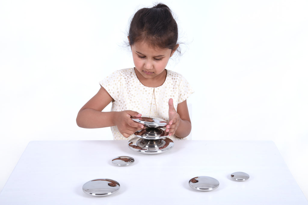 Seven round silver sensory metal buttons on a tabletop with a stacked holder
