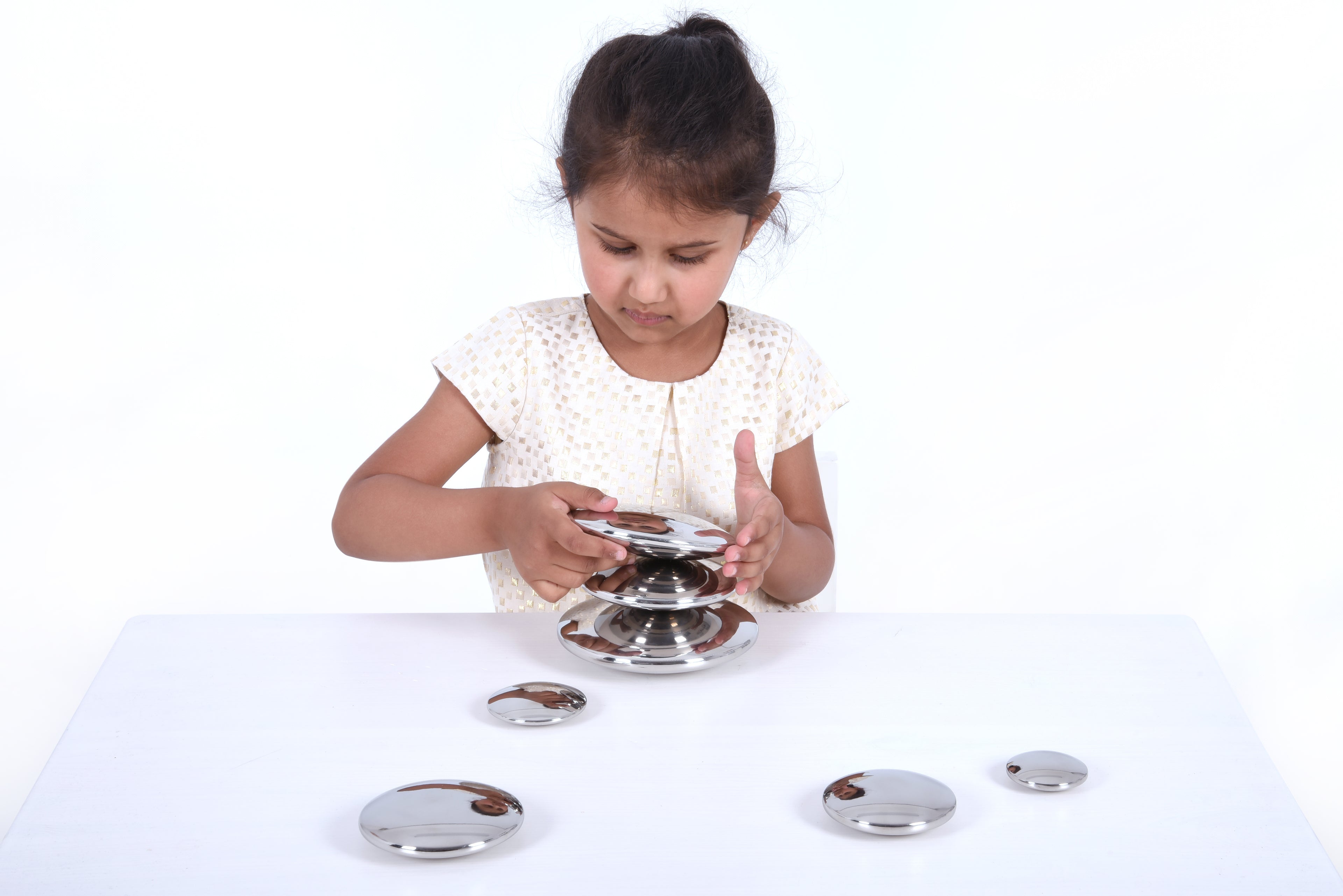 Seven round silver sensory metal buttons on a tabletop with a stacked holder