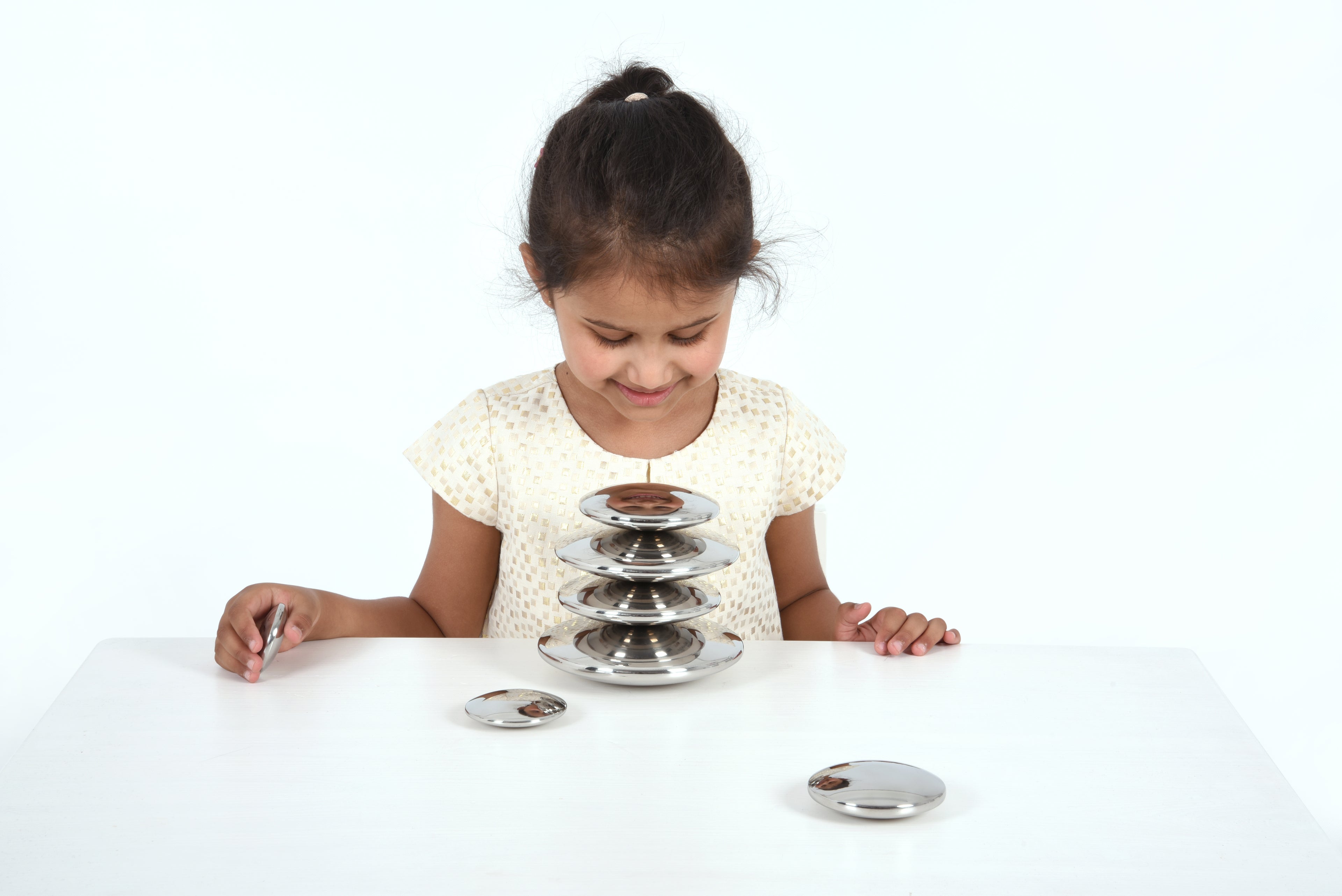 Seven round silver sensory metal buttons with a stacked base on a table