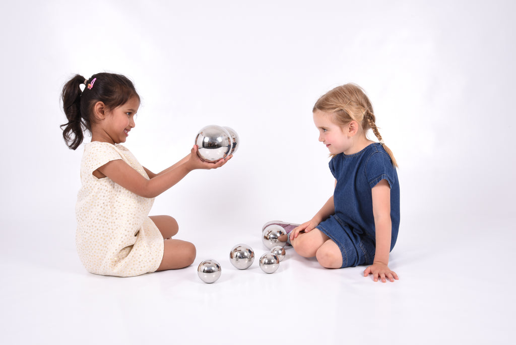 Set of 7 shiny silver steel sound balls in children’s hands, some on floor
