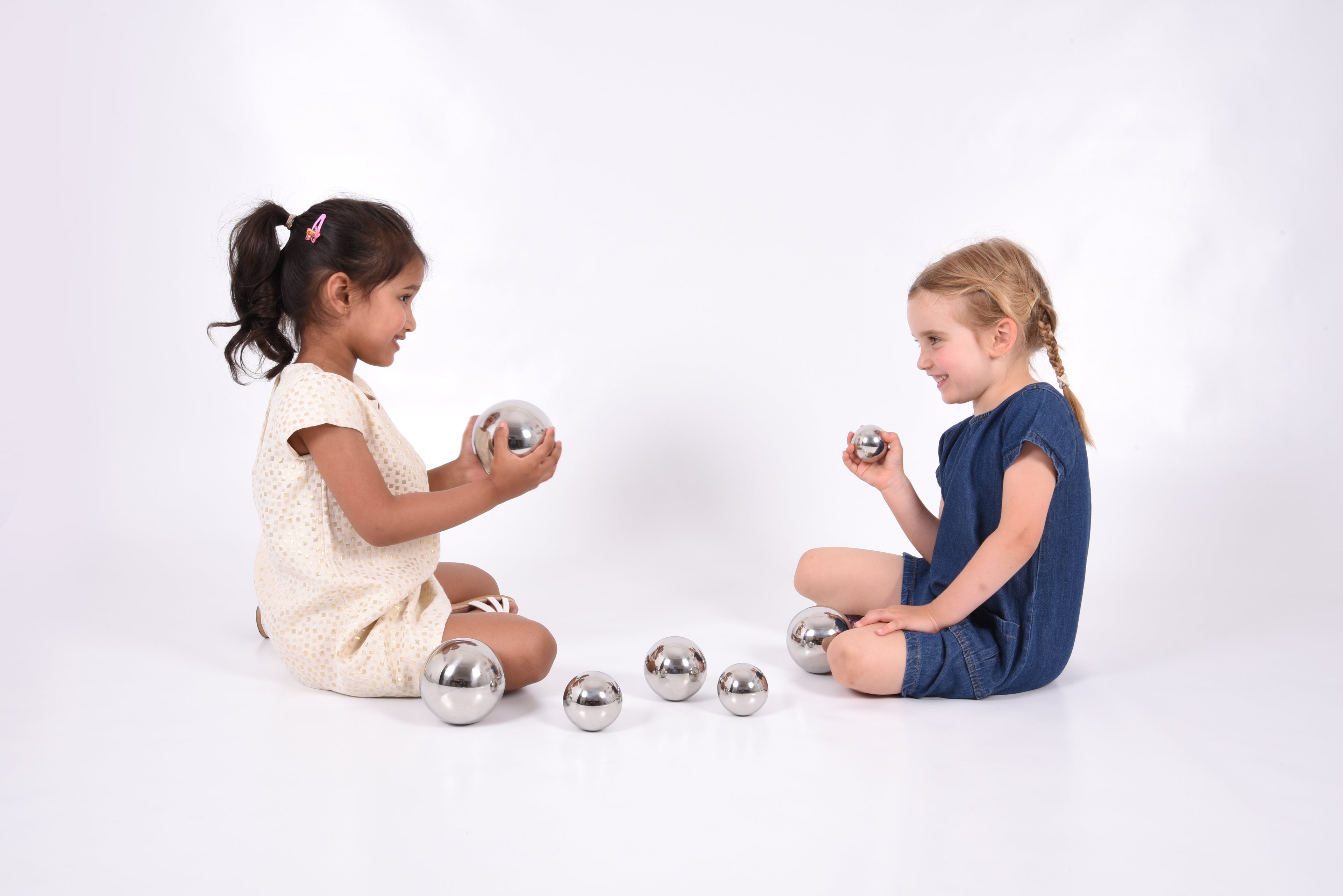 Set of 7 shiny silver steel sound balls arranged on the floor, children playing