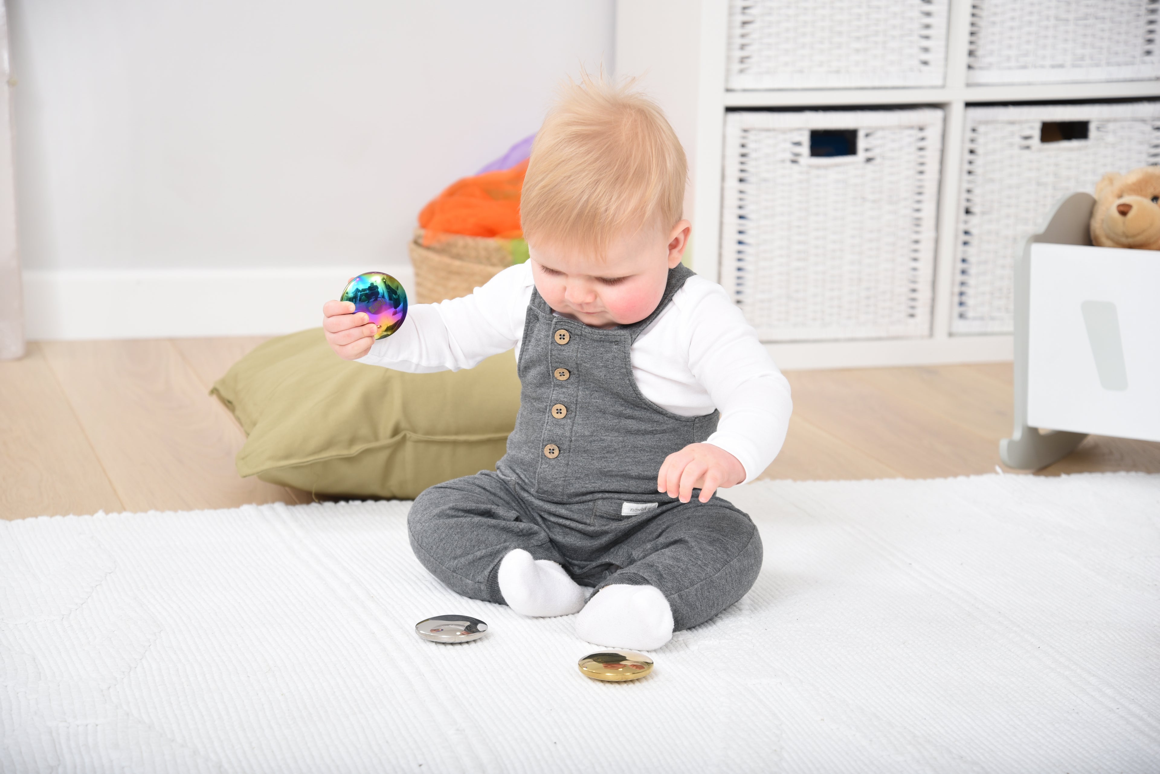 Child playing with three sensory sound buttons: iridescent, silver, and cream