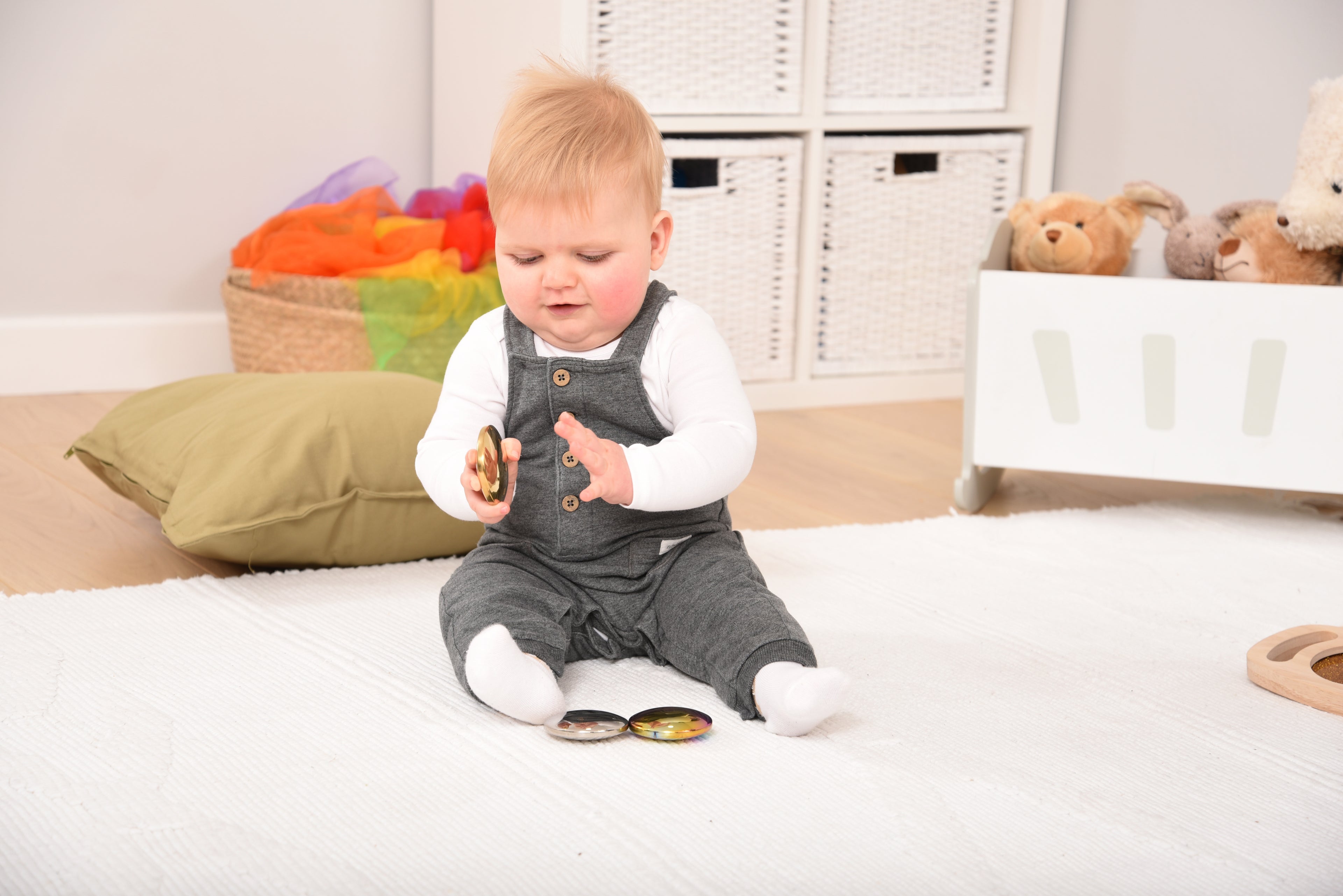 Three sensory sound buttons on a play mat: rainbow iridescent and metallic silver
