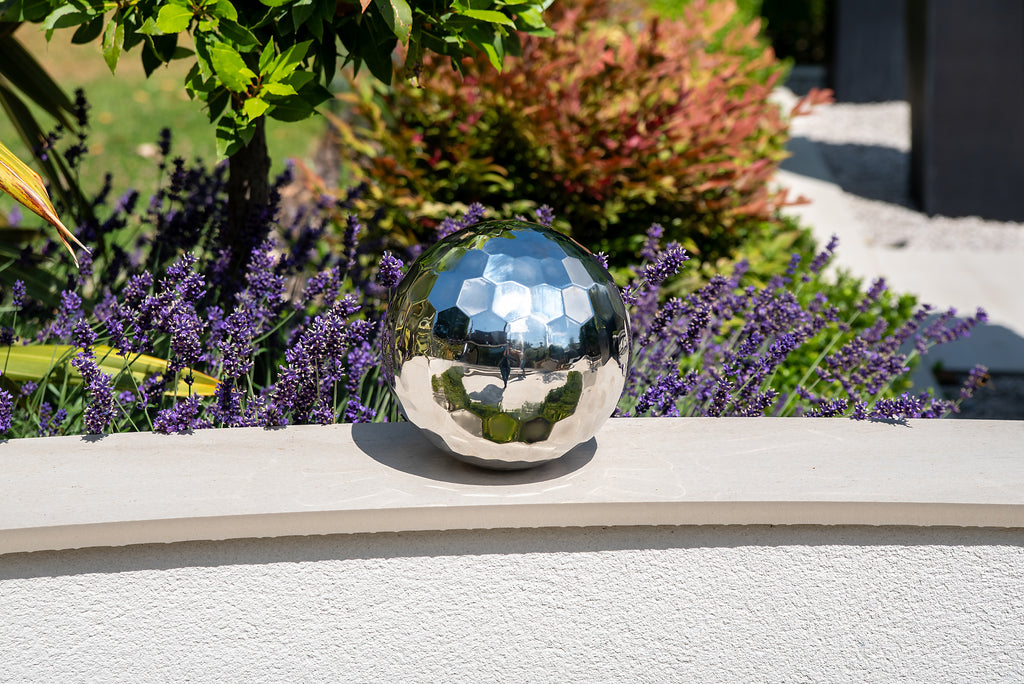 Reflective steel tumble ball with mirrored facets on a patio step