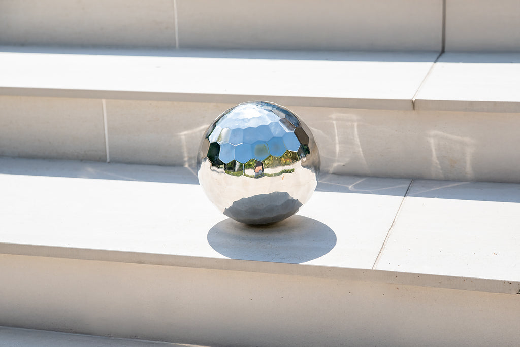 Reflective silver steel tumble ball resting on a tiled ledge